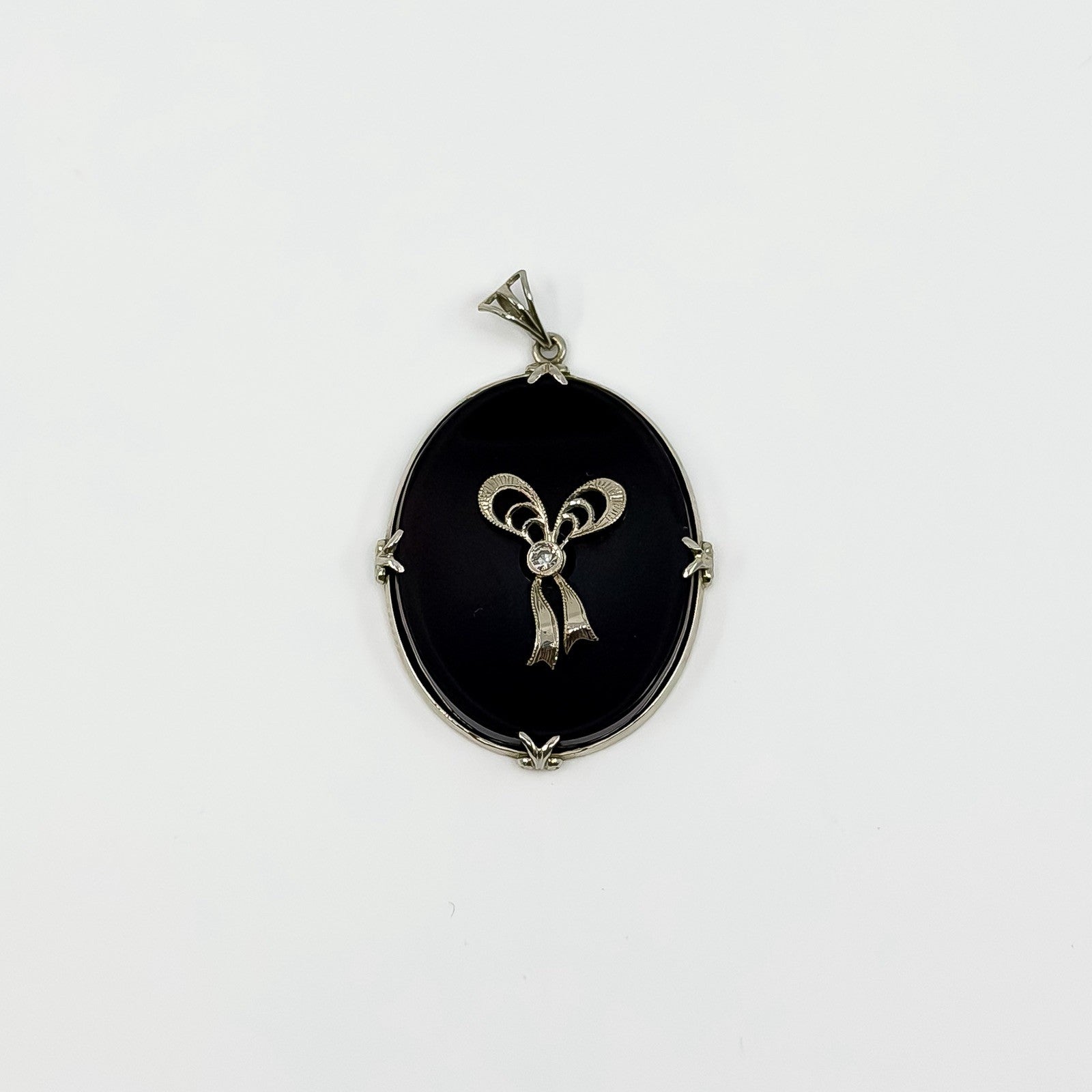 Vintage 14ct white gold black onyx pendant with diamond bow centre on white background.