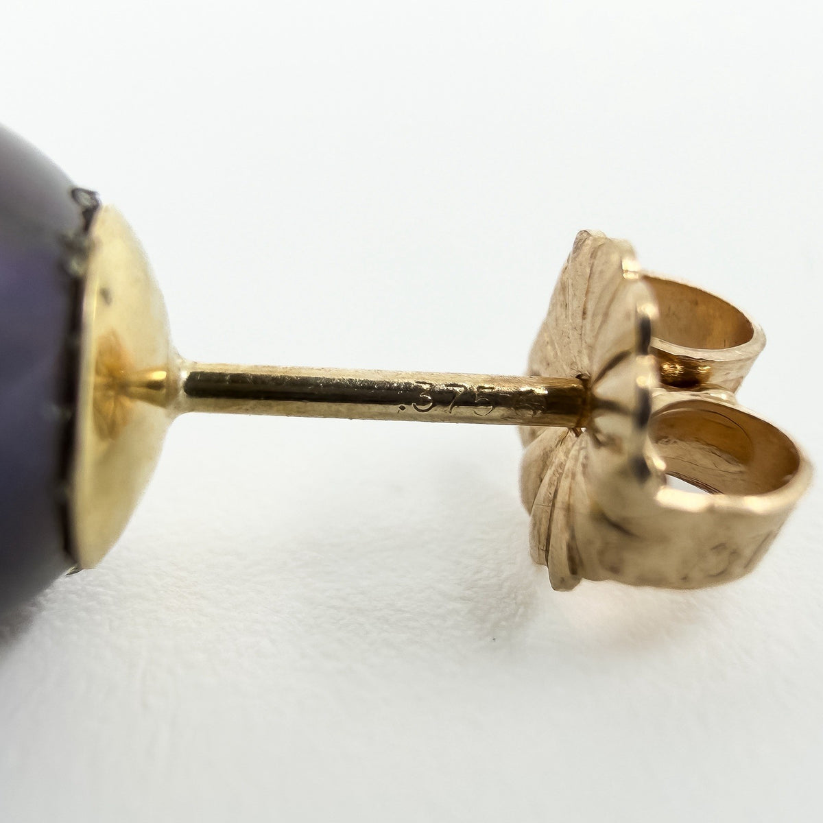 Macro view of a 9ct gold earring post stamped 375 beside a cultured black pearl