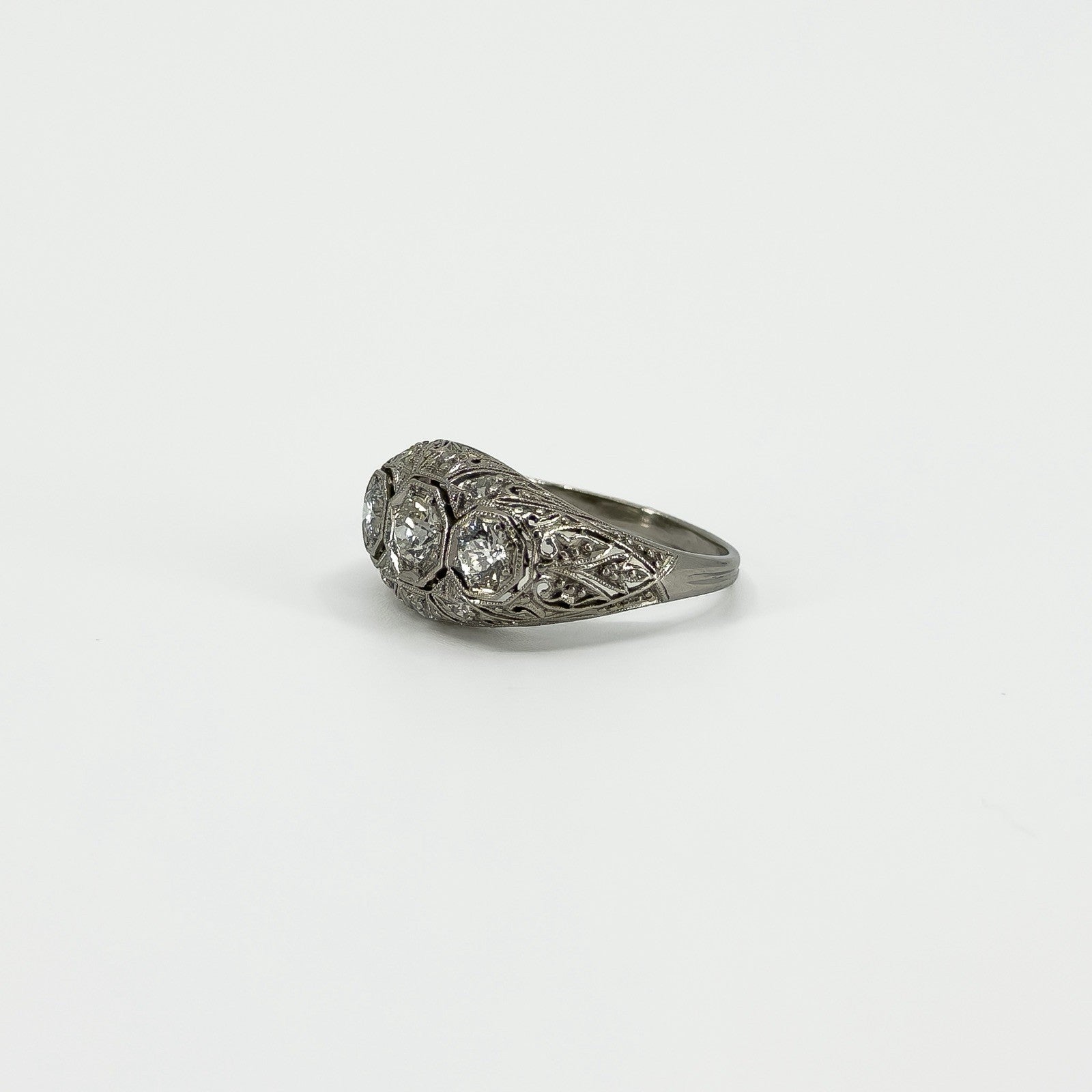 Angled side view of Art Deco platinum diamond trilogy ring with filigree detail