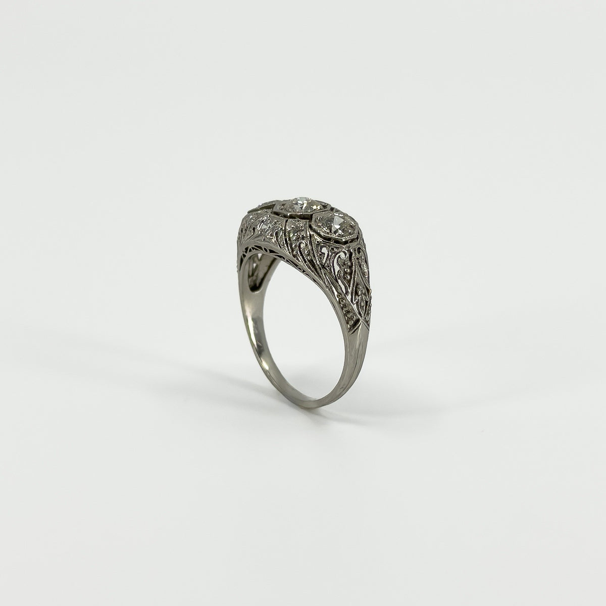 Angled view of Art Deco platinum diamond trilogy ring showing pierced filigree shoulders