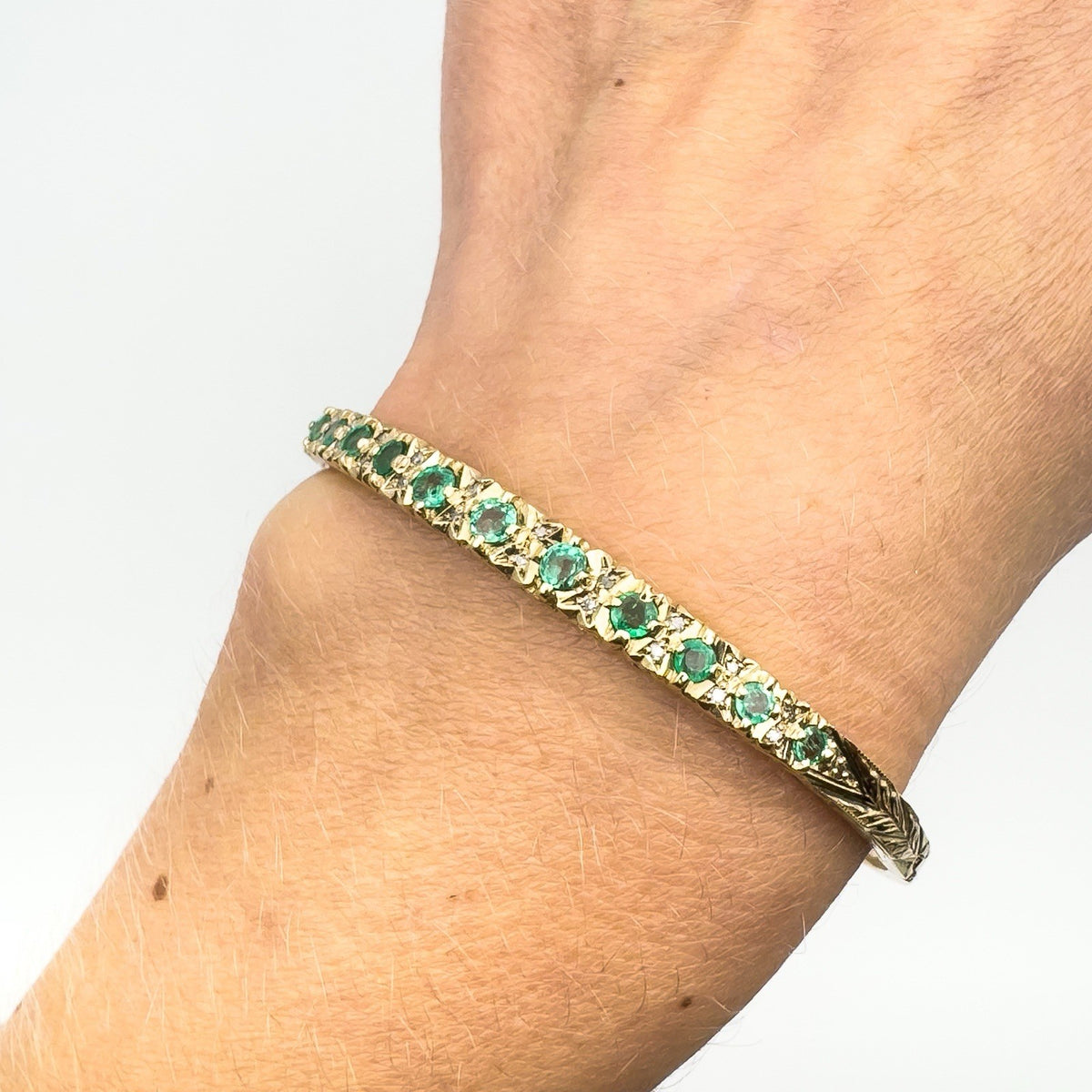 Close-up of vintage gold bangle with emeralds worn on wrist
