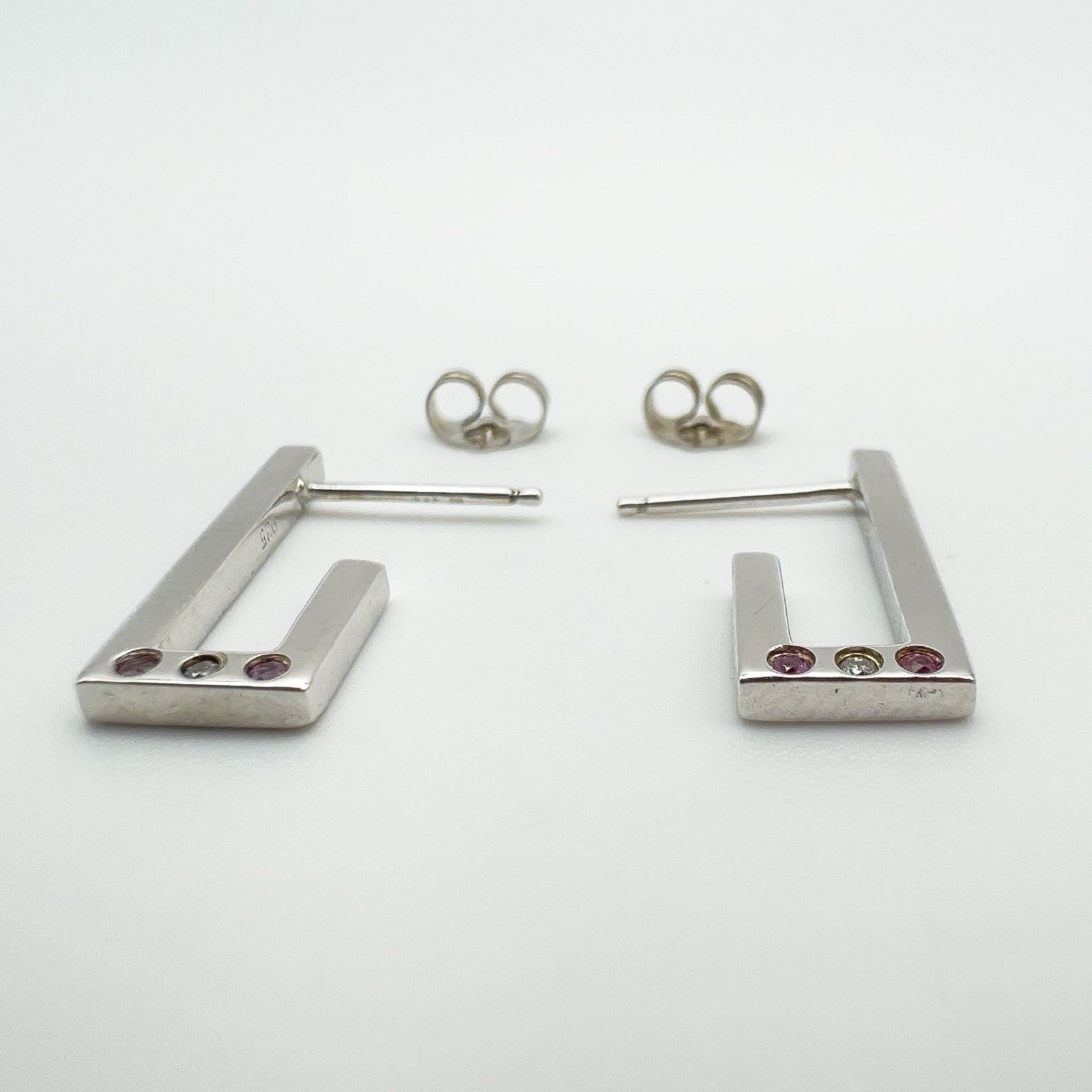 Detail view of bezel set pink sapphires and diamond on sterling silver J hoop earrings