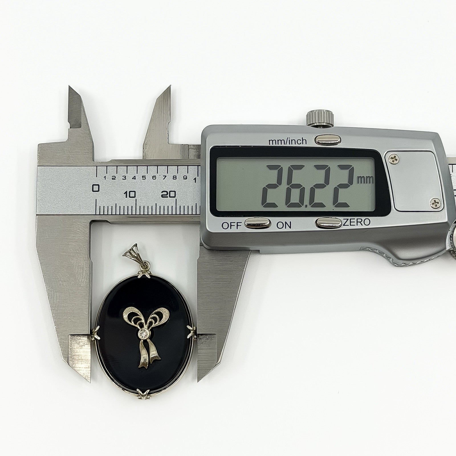 Digital caliper measuring the black onyx and diamond bow pendant width at approximately 26.22mm.