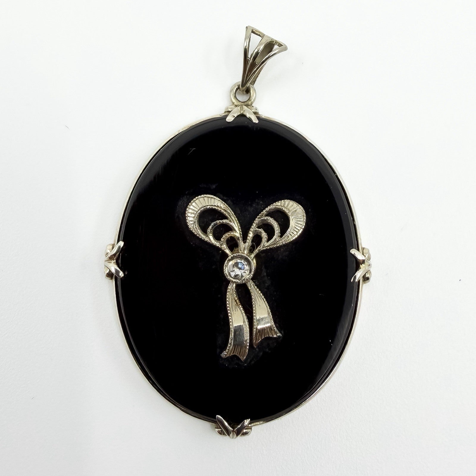 Close up of vintage 14ct white gold black onyx pendant with bow design and centre diamond.