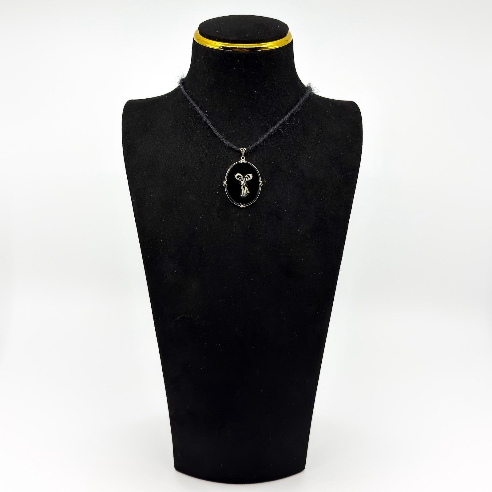 Vintage black onyx and diamond bow pendant shown on a black display bust.