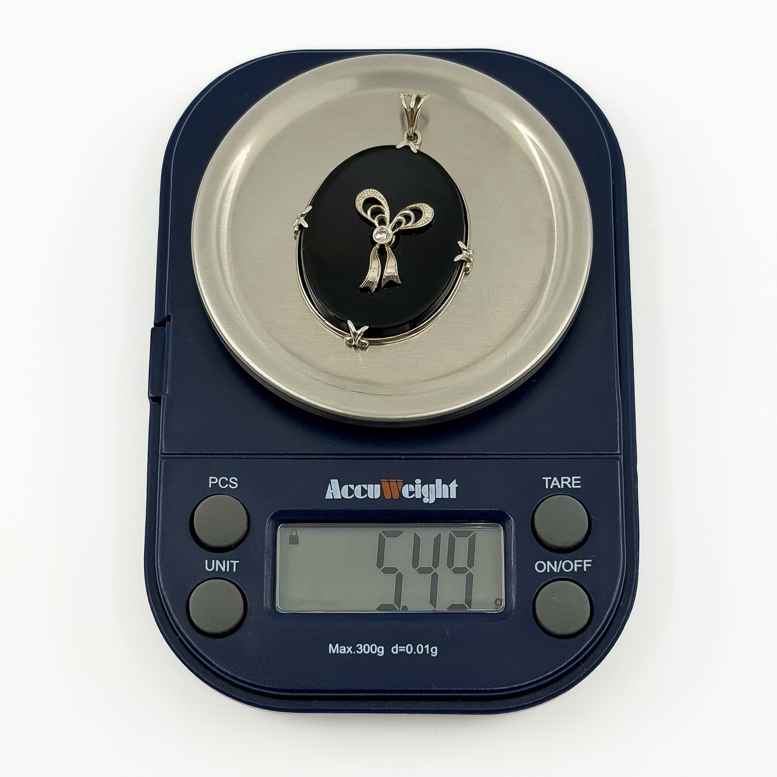 Vintage 14ct white gold black onyx and diamond bow pendant shown on scales weighing approximately 5.49g.