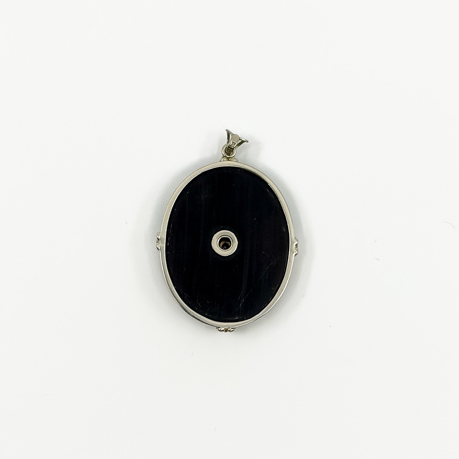 Back of black onyx pendant showing plain oval reverse with centre fitting and white gold frame.