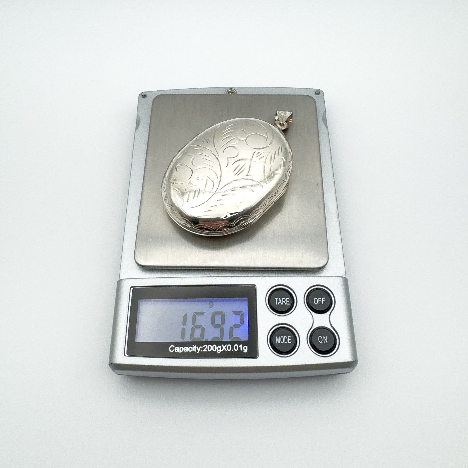 Large vintage sterling silver oval locket on digital scale showing weight of 16.92 grams.