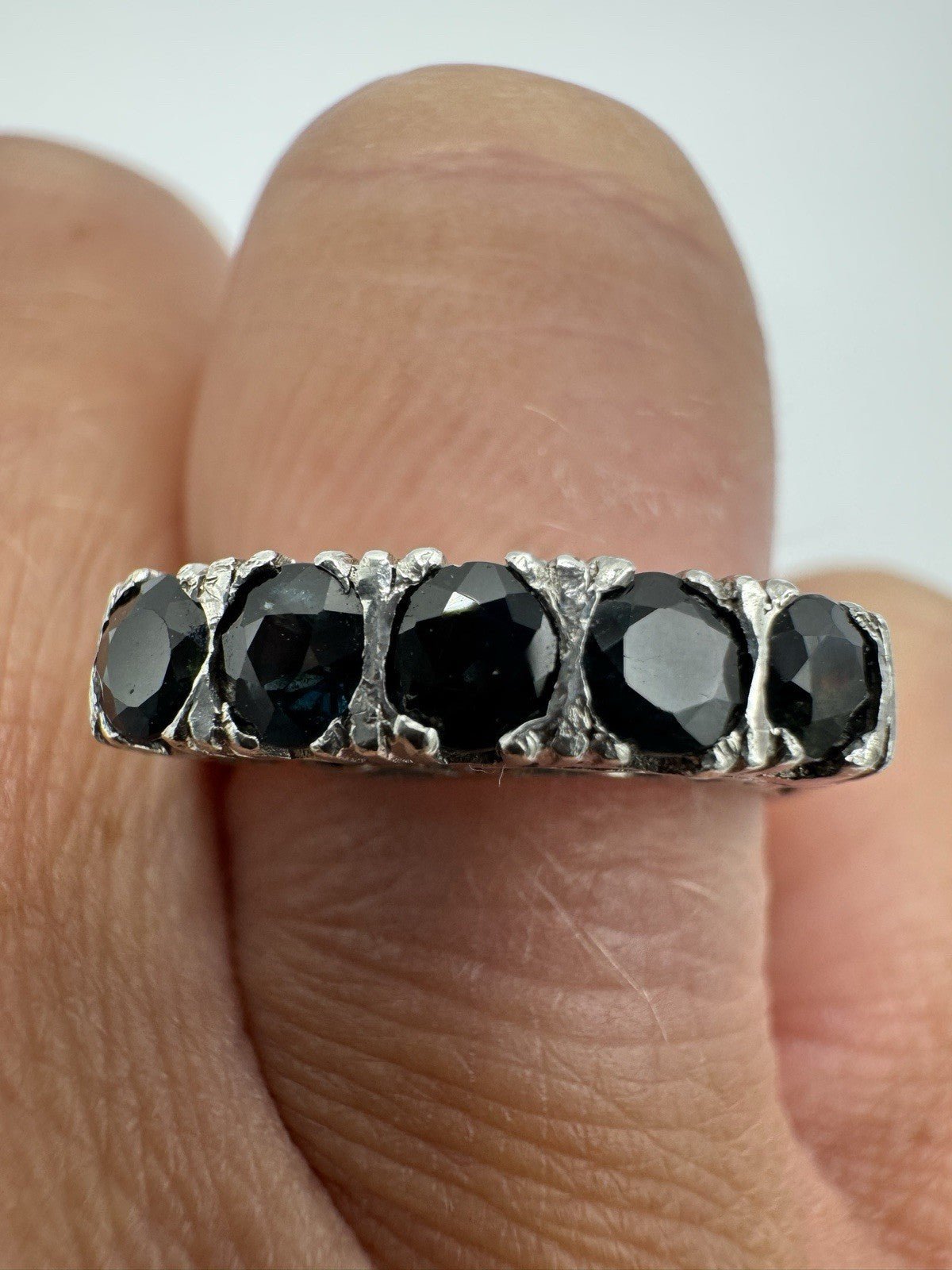 Five dark blue sapphires in claw settings on sterling silver band shown up close