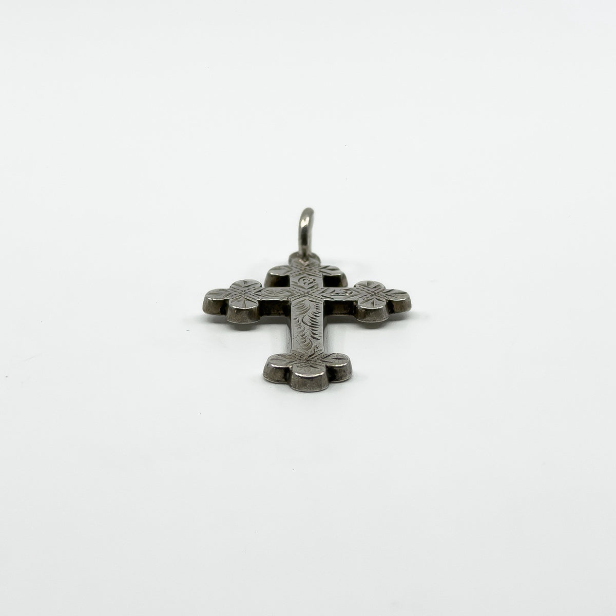 Low side view of antique Victorian silver cross pendant showing engraved face and depth