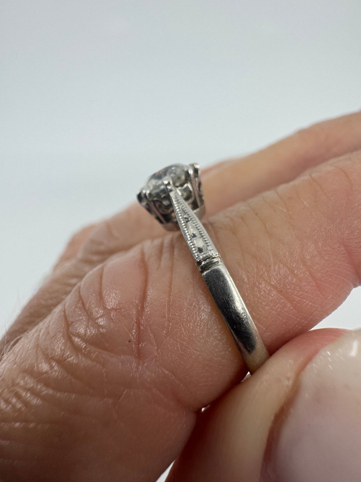 Side view of antique platinum old-cut diamond solitaire ring worn on hand with engraved shoulder detail