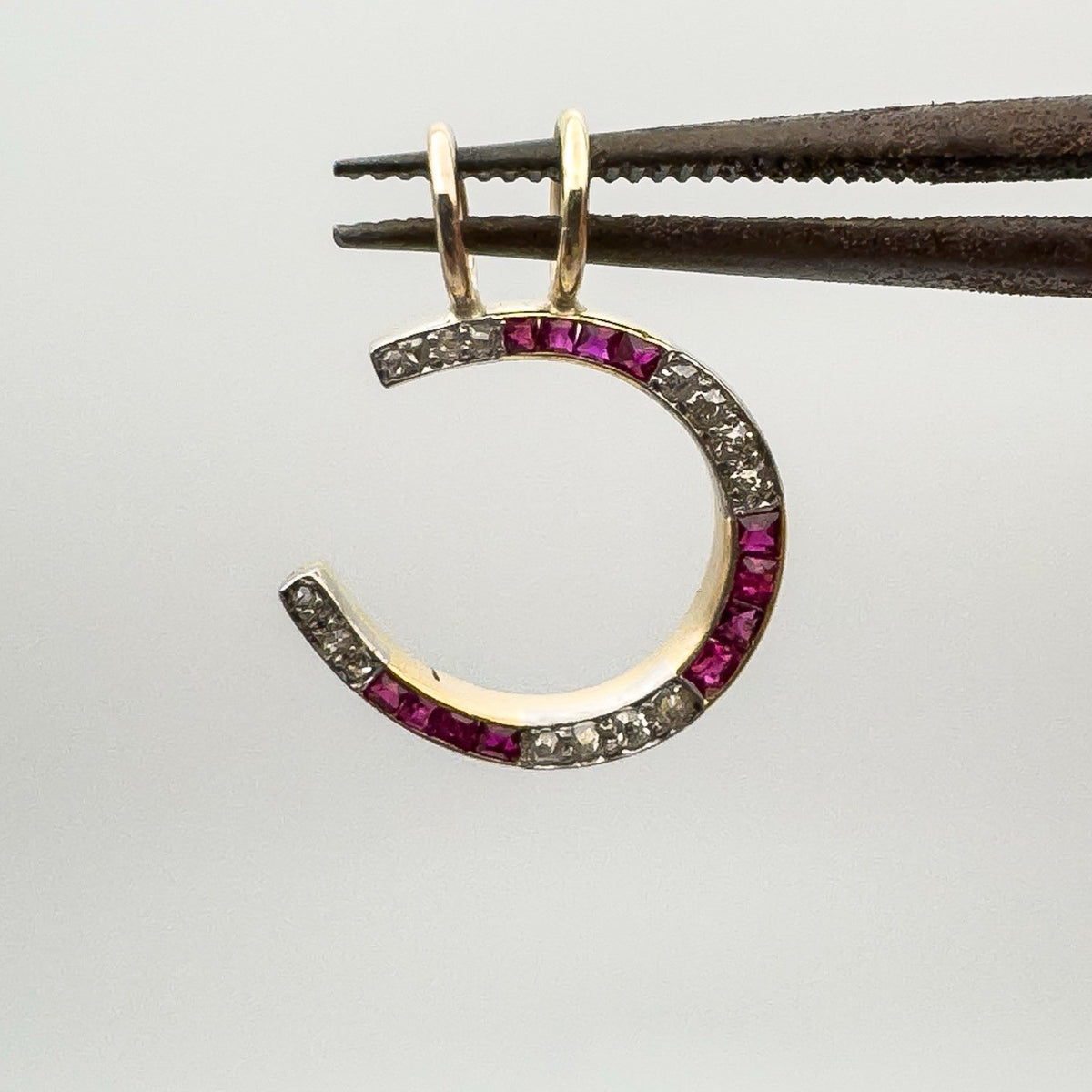 Front view of ruby and diamond horseshoe charm held up for detail