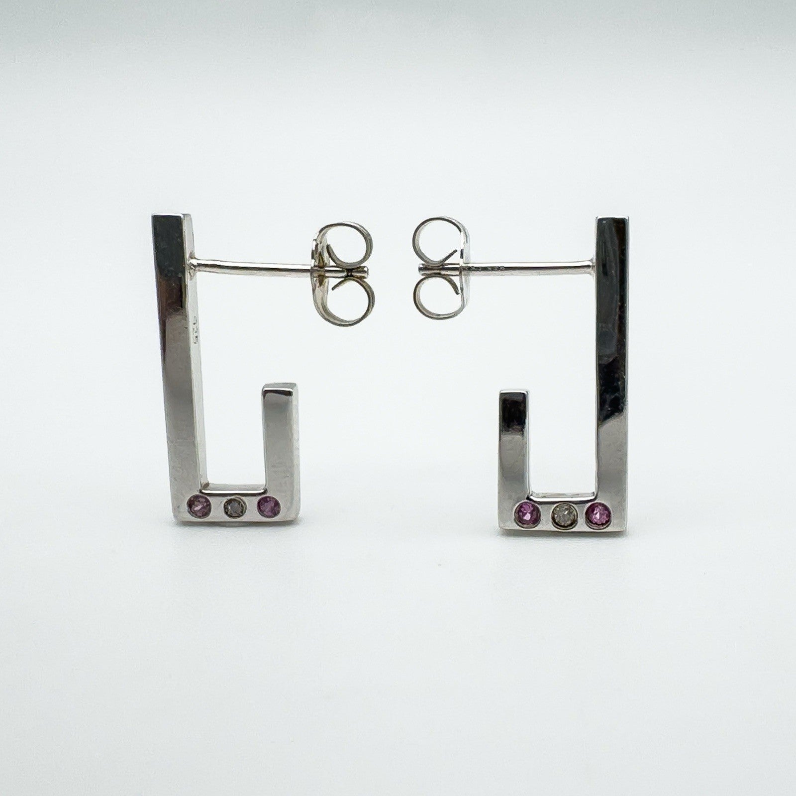 Sterling silver J hoop earrings showing pink sapphires and diamond bezel set at the base