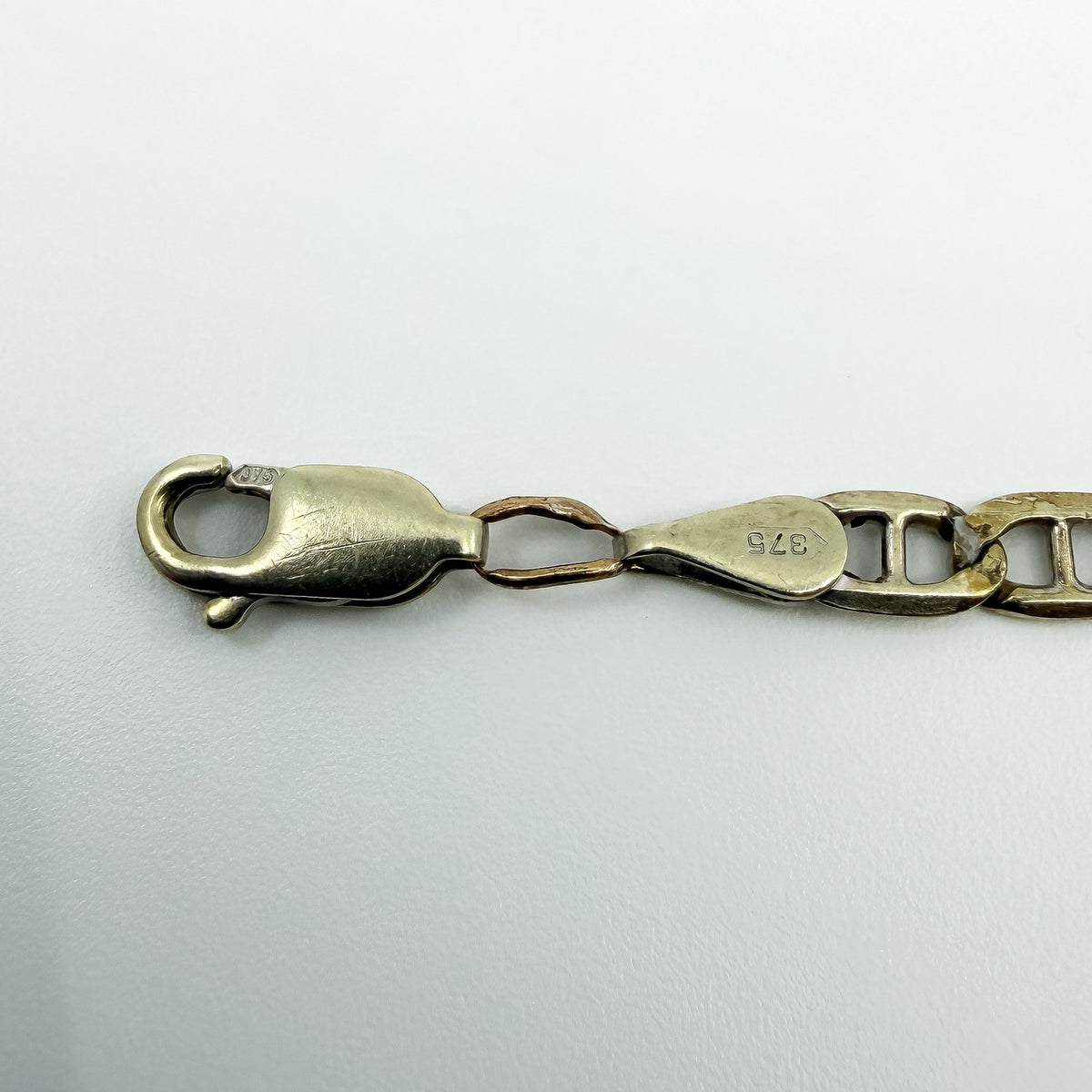 Close up of the lobster clasp, 375 stamps and connecting link on a 9ct white gold mariner bracelet