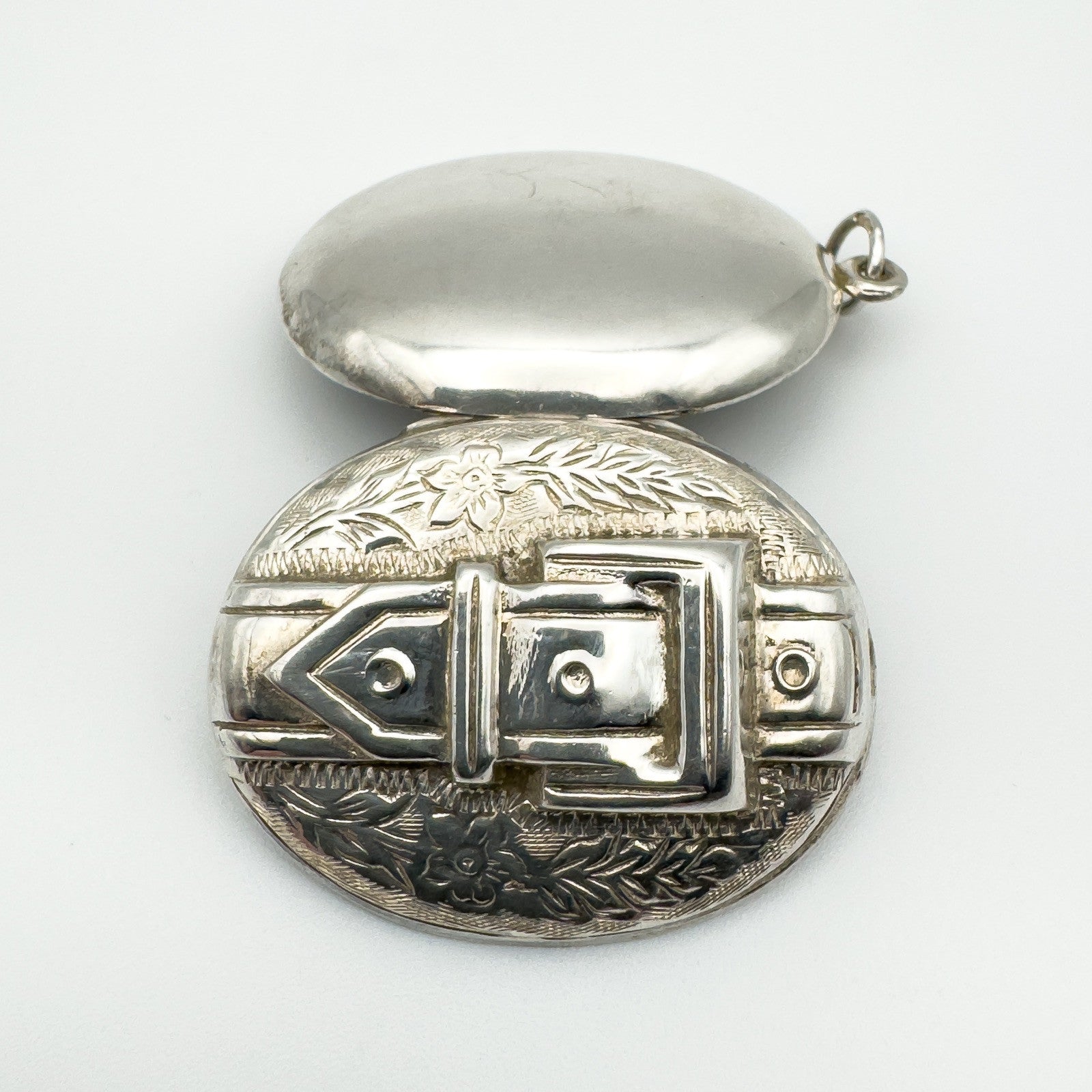 Vintage silver buckle locket open to show inner hinge and foliate design