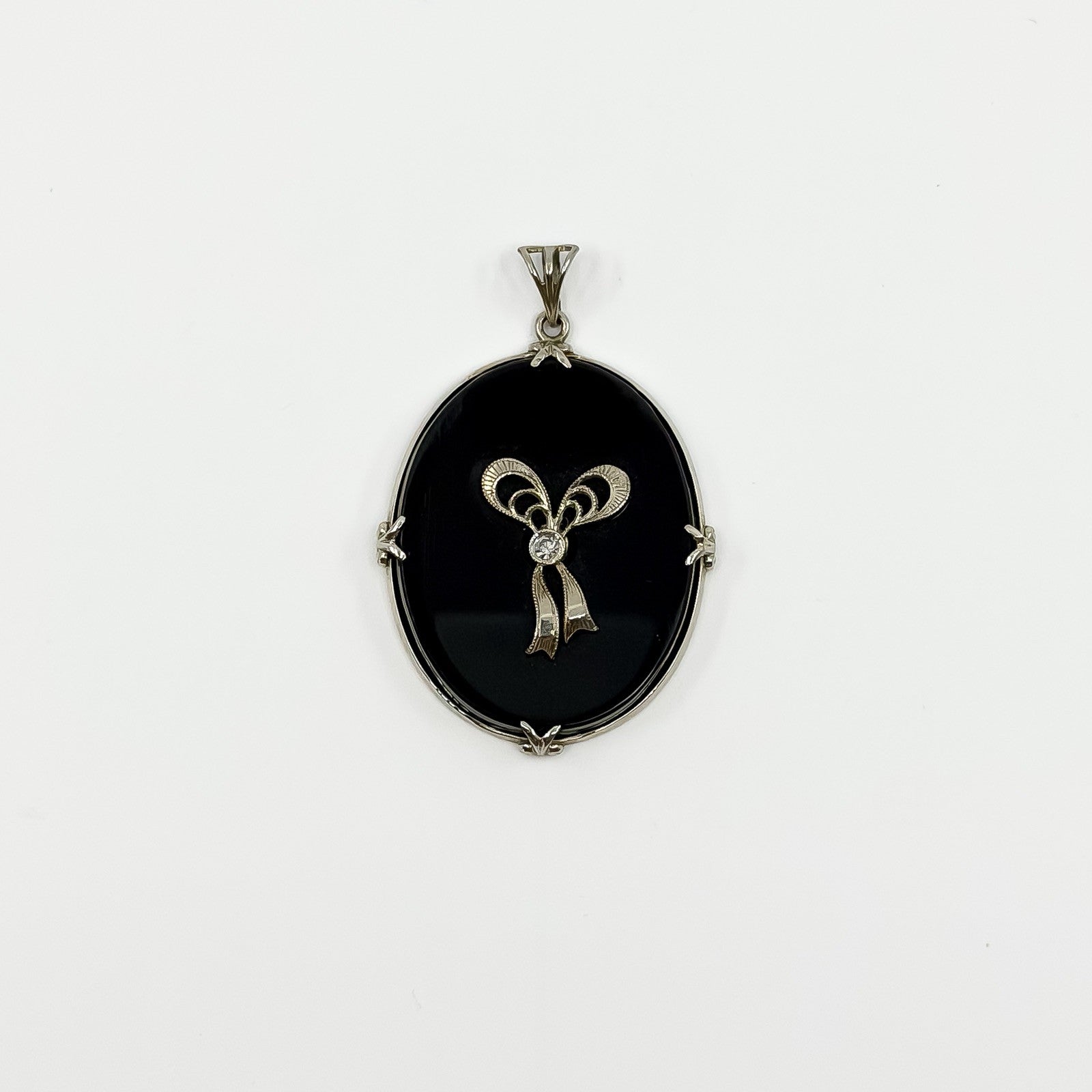 Full front view of oval black onyx and diamond bow pendant with bail and white gold frame.