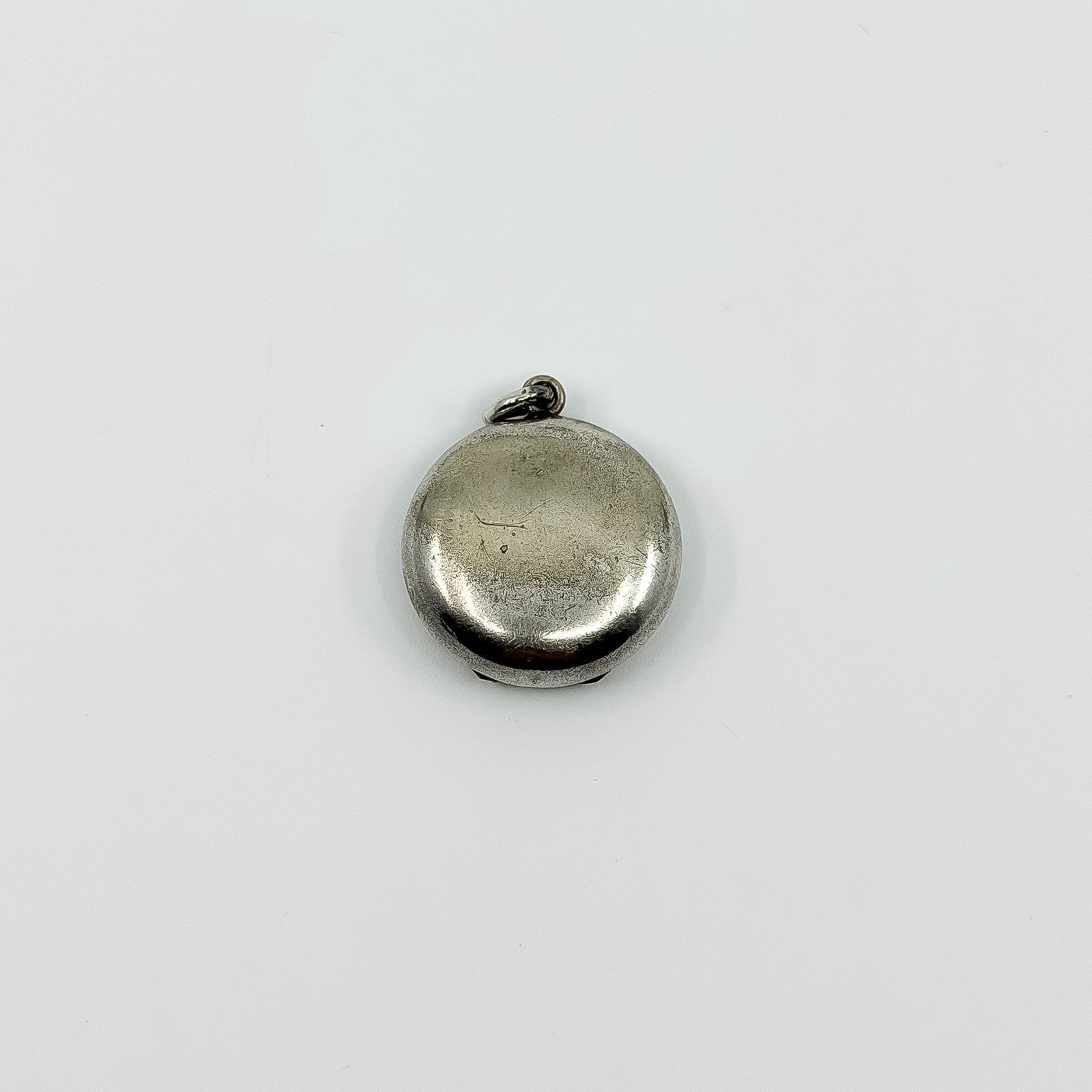Plain back of vintage sterling silver Virgin Mary photo locket pendant showing surface wear.