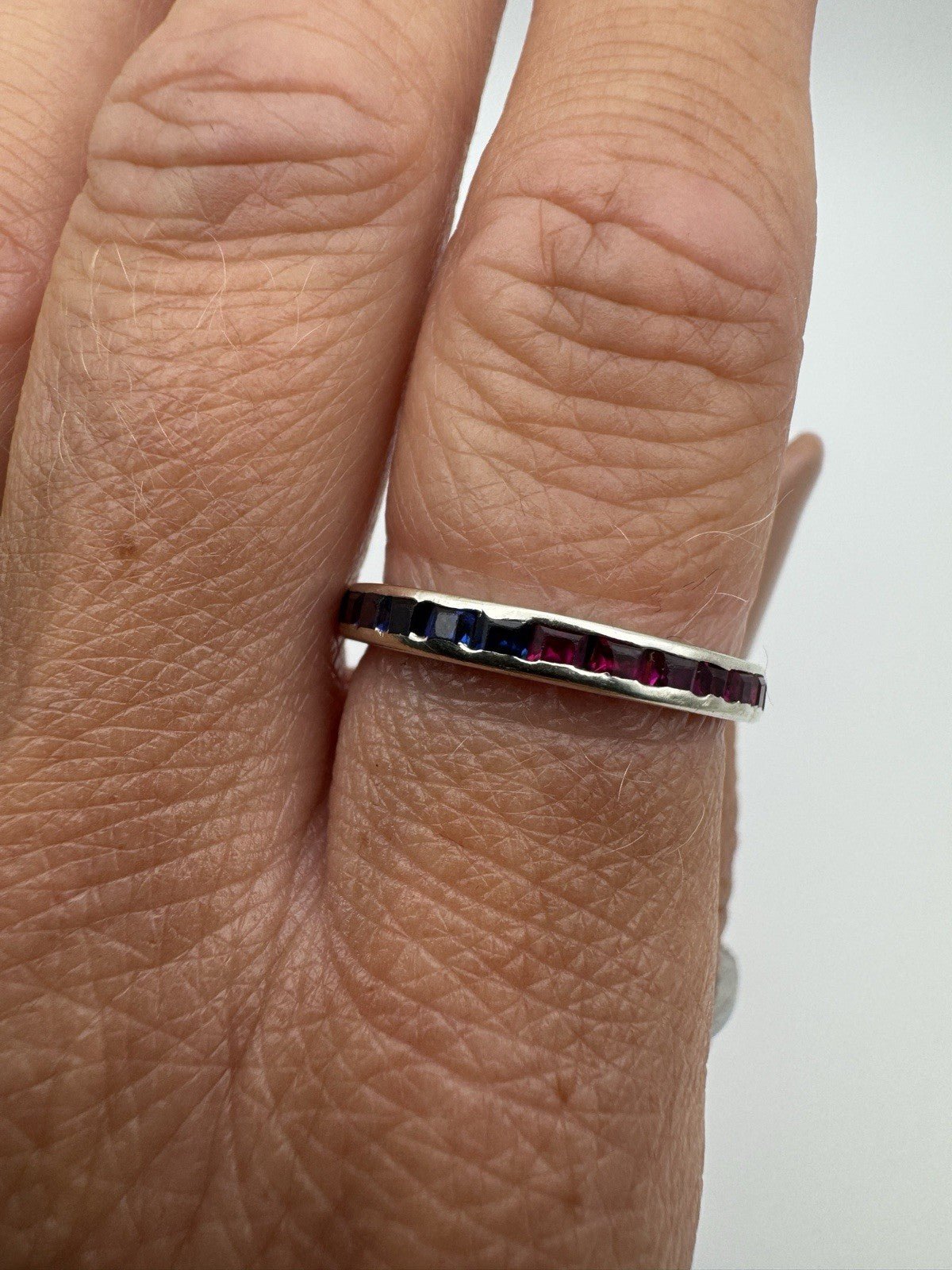 Channel set sapphire and ruby eternity ring worn on finger side profile