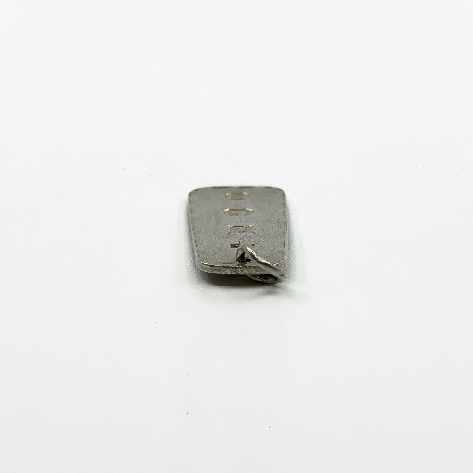 Side view of vintage sterling silver ingot pendant showing slim rectangular shape and jump ring.