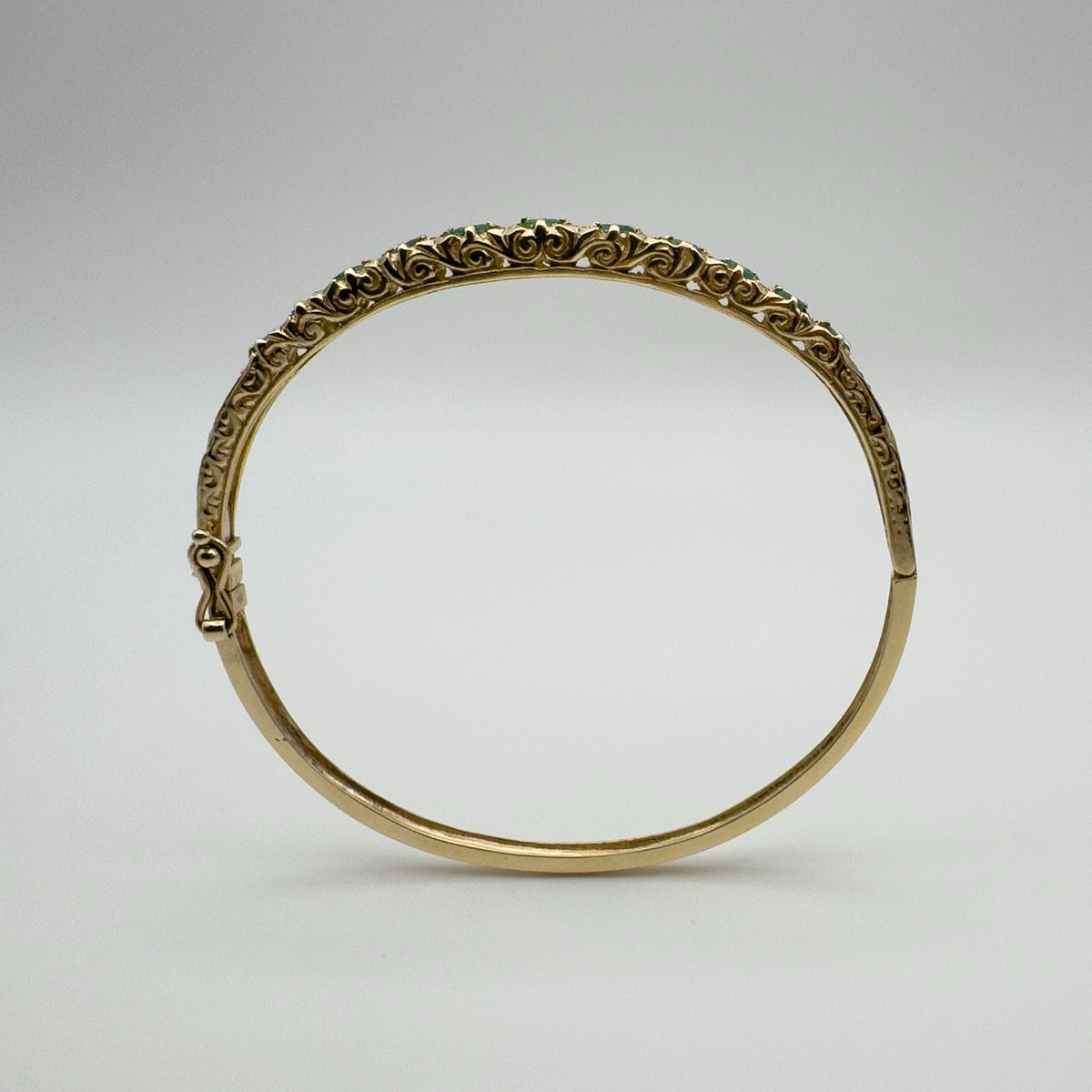 Side view of vintage gold emerald bangle with floral engraving and push clasp
