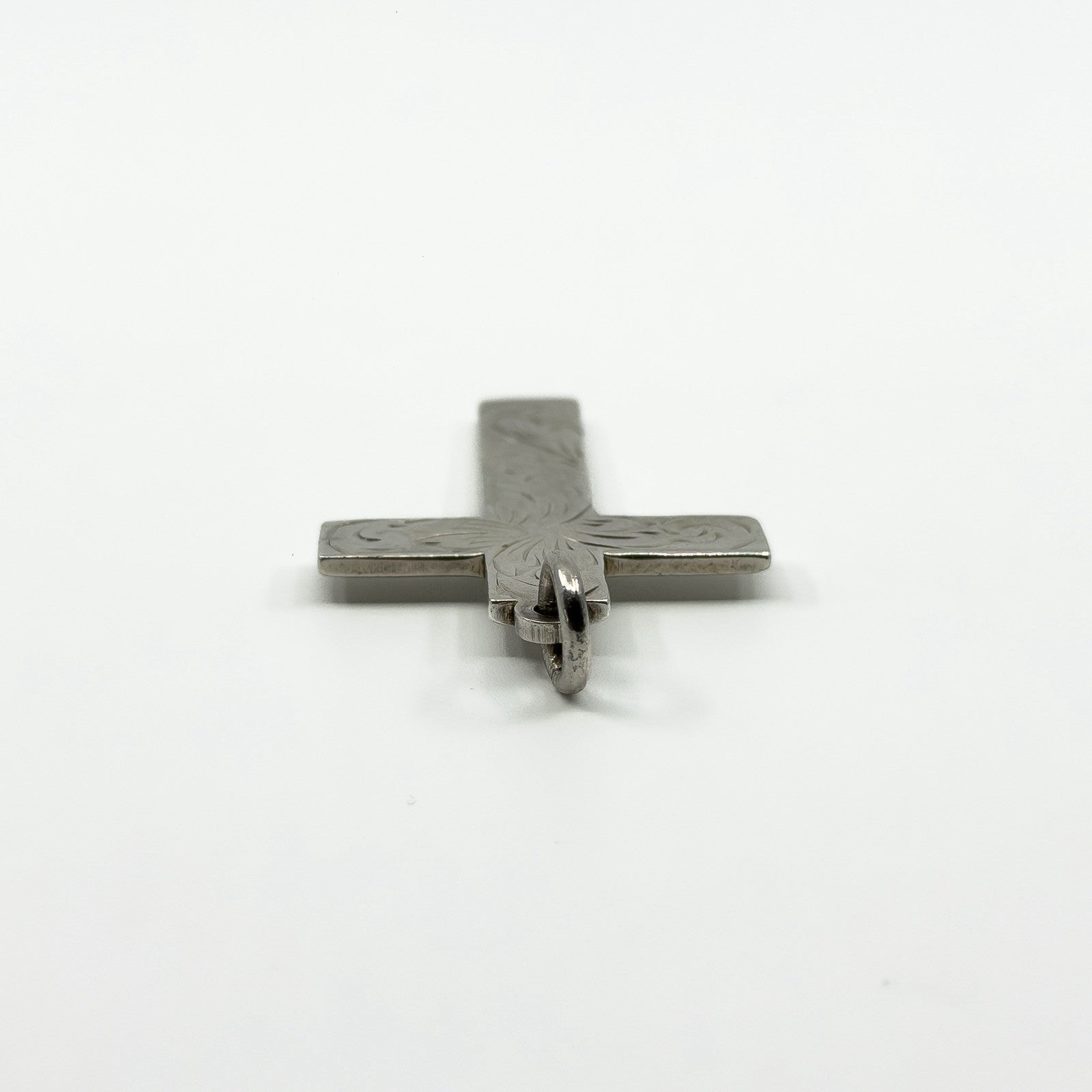 Low angle view of the sterling silver cross pendant showing the bail and thickness.
