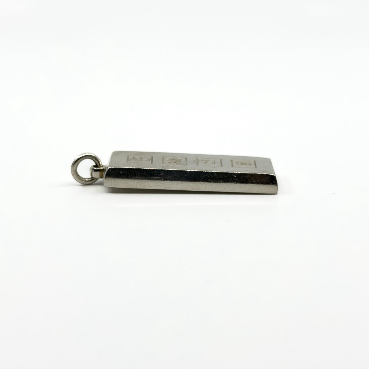 Angled side view of the silver ingot pendant showing the thick edge and hallmark panel.