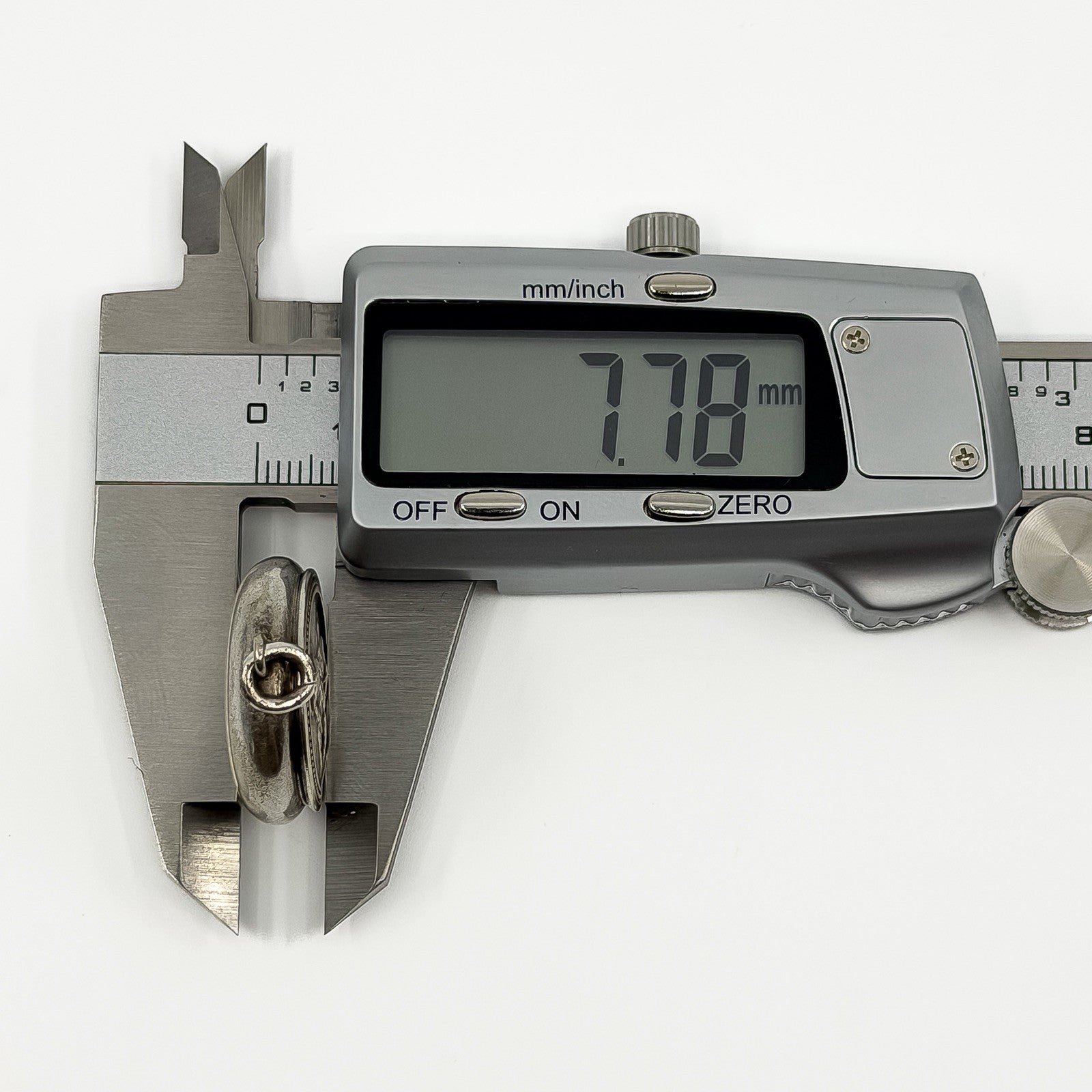 Digital caliper measuring the vintage sterling silver Virgin Mary photo locket depth at approximately 7.78mm.