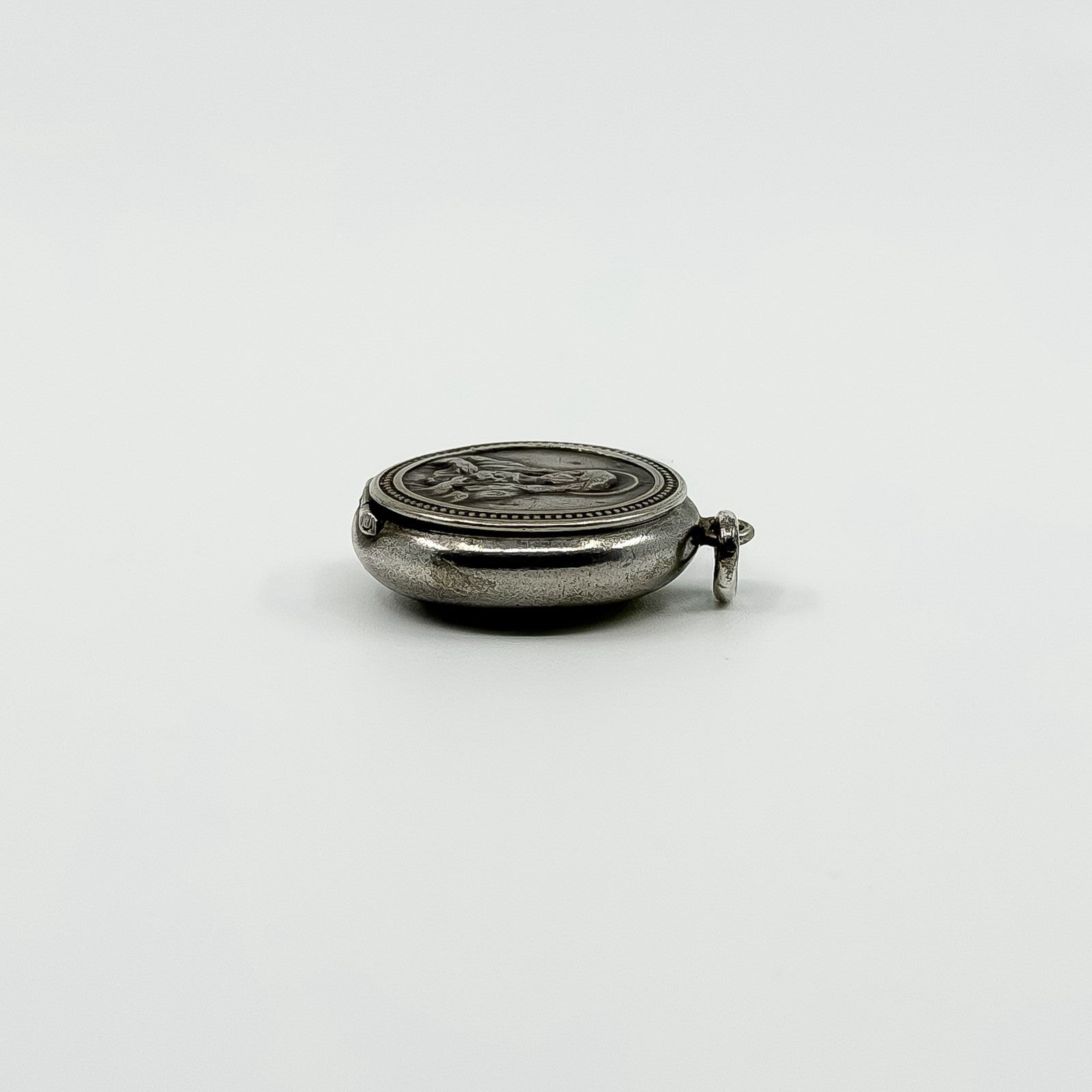 Side view of vintage sterling silver Virgin Mary photo locket with jump ring and raised front detail.