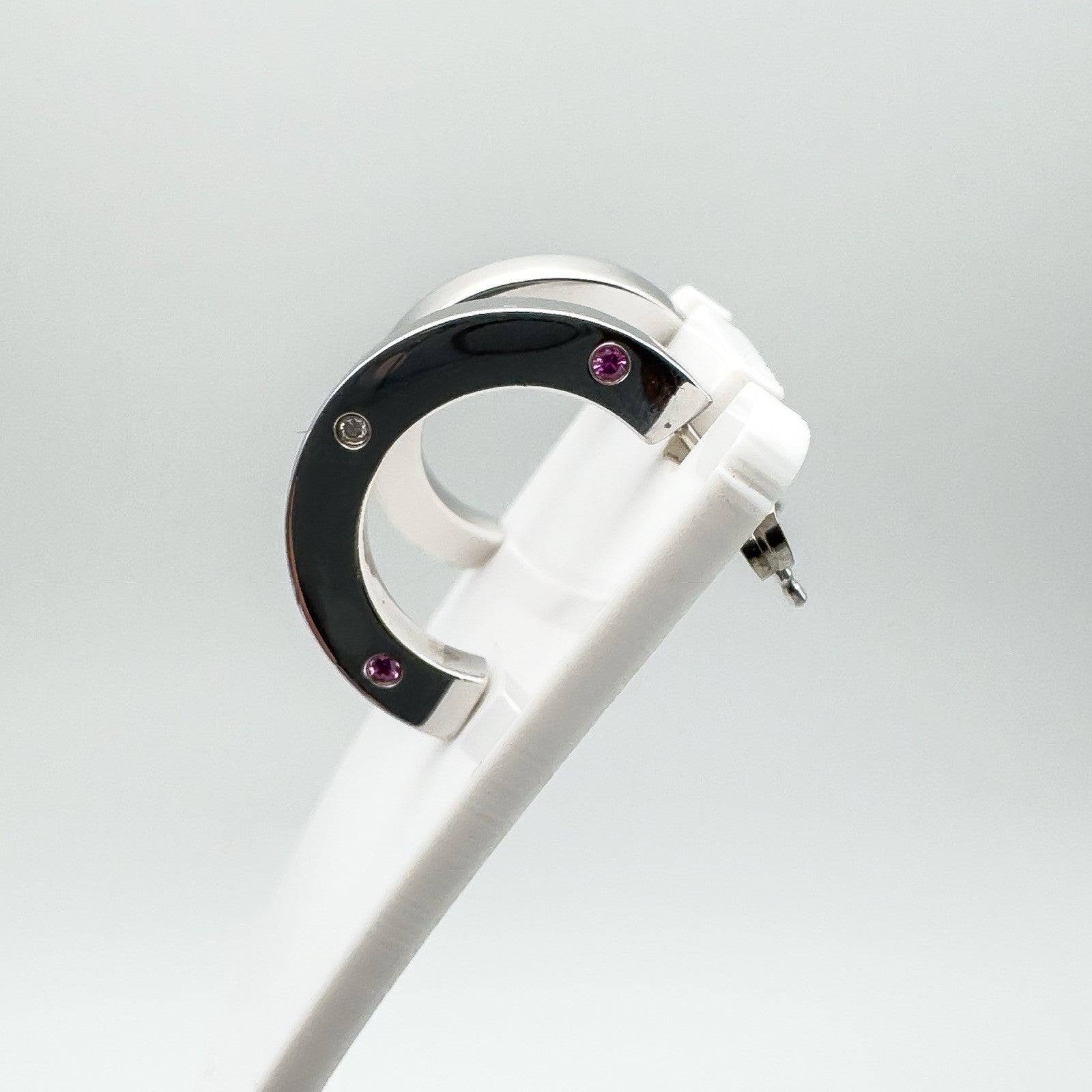 Single earring shown on white display, highlighting bezel set stones and polished silver finish