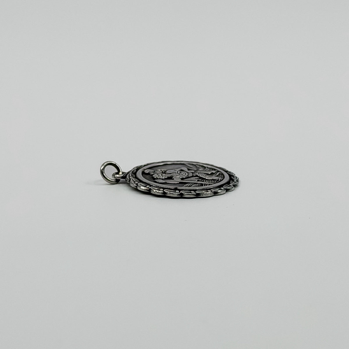 Low side view of vintage sterling silver St Christopher pendant charm showing its slim profile.