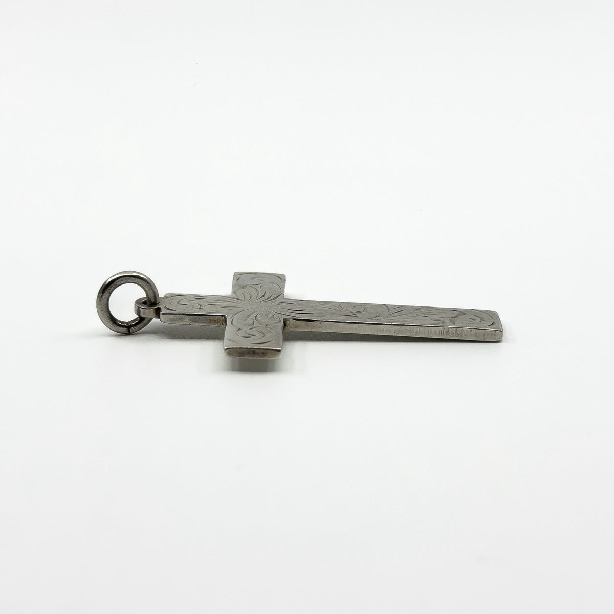 Side profile of the engraved sterling silver cross pendant laid flat on a white background.