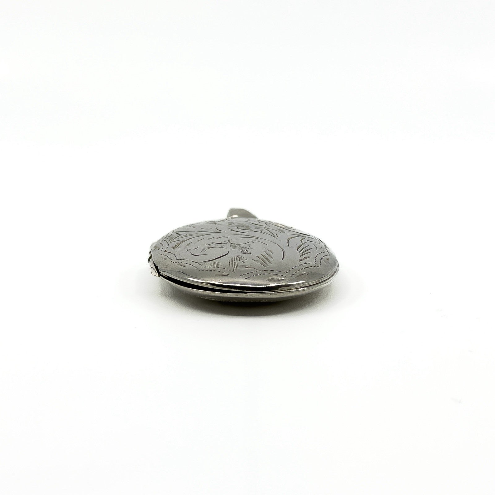 Side view of a vintage sterling silver oval photo locket showing engraved detail and rounded depth