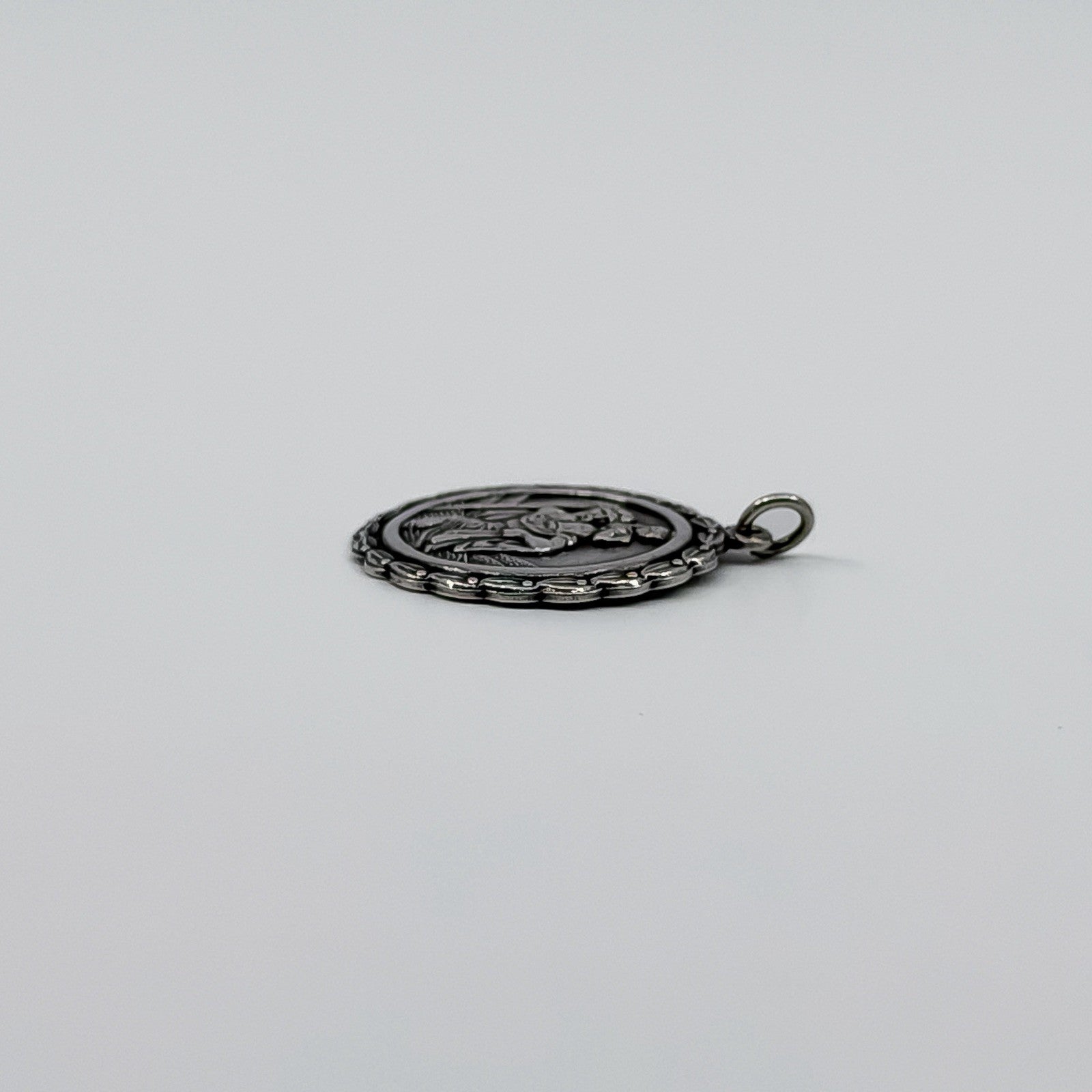 Side view of sterling silver St Christopher pendant charm showing the textured edge and jump ring.