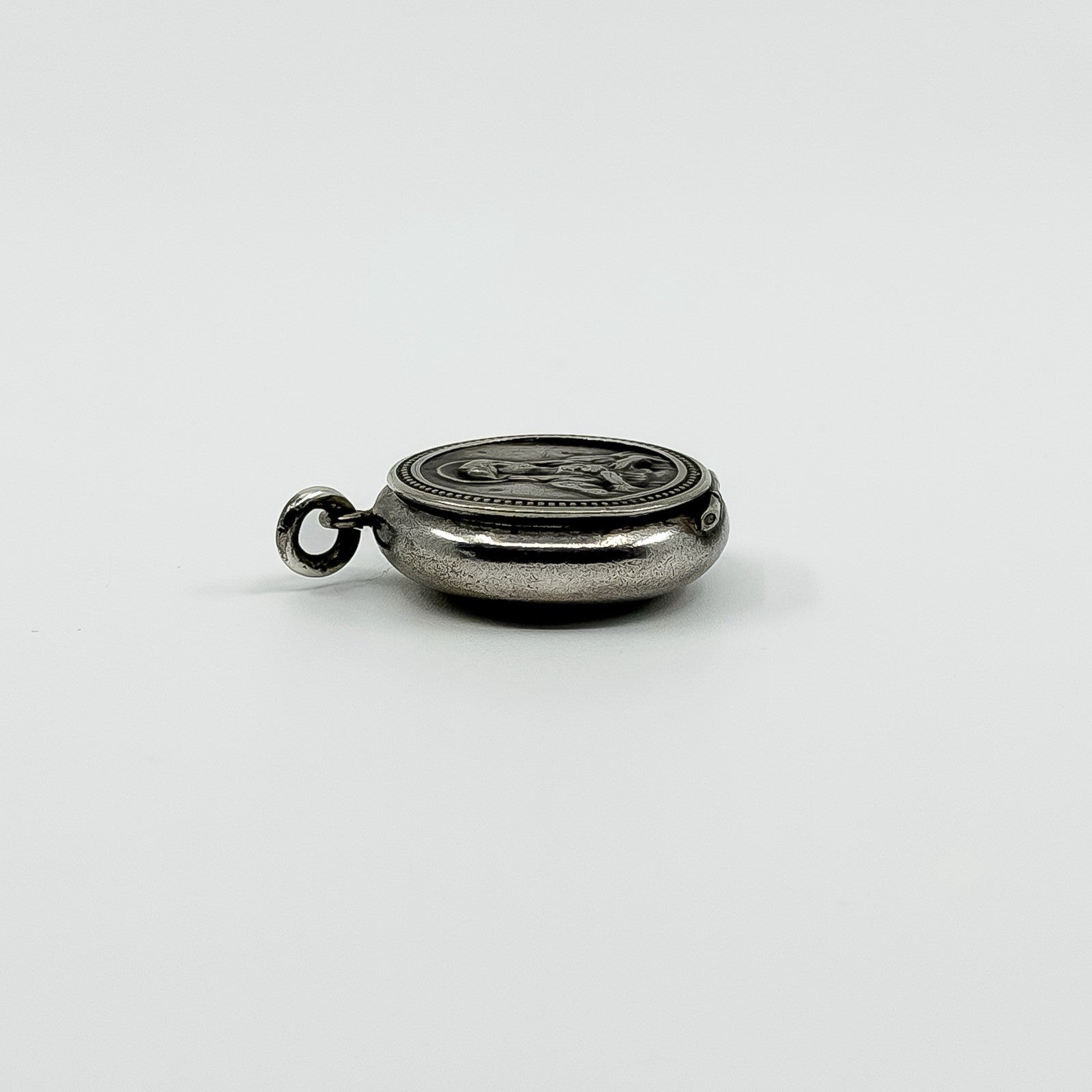 Side view of vintage sterling silver Virgin Mary photo locket pendant showing its rounded shape.