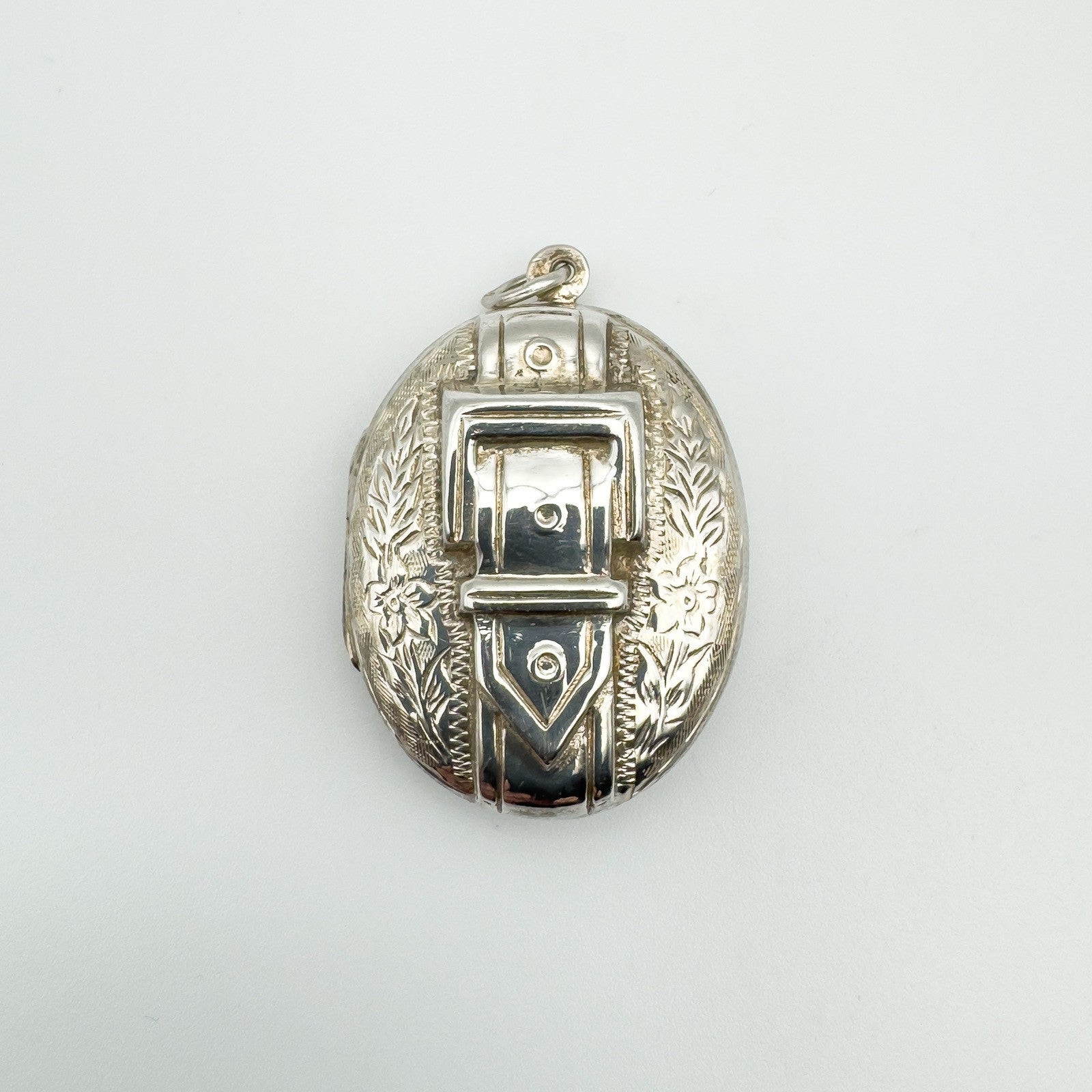 Overhead view of vintage silver buckle locket with floral engraving