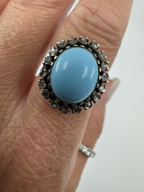 Close up of the turquoise cabochon and rough cut diamond halo ring worn on the hand