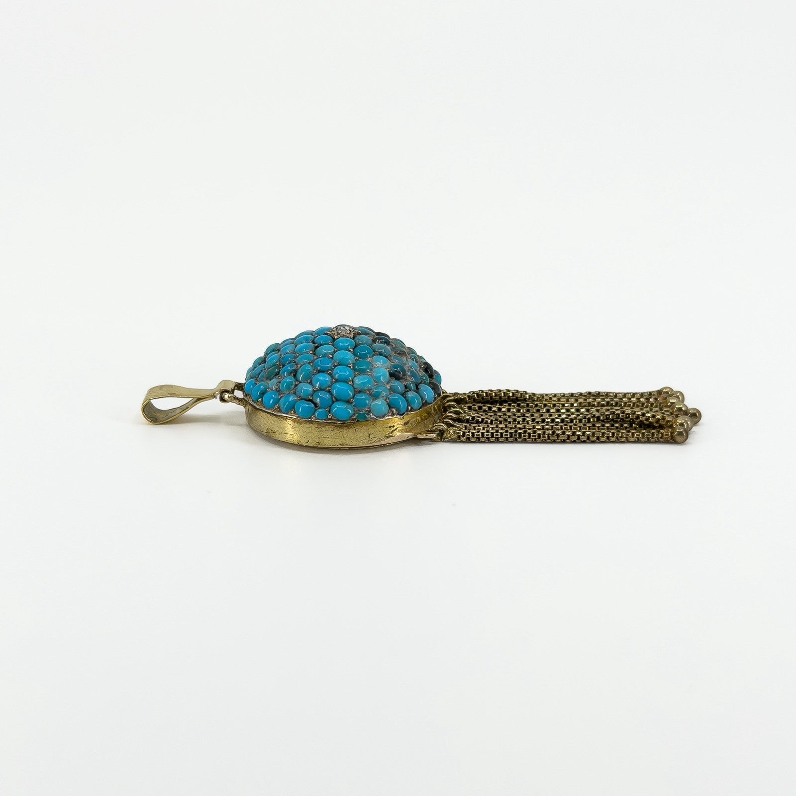 Side profile of antique 18ct gold turquoise locket showing the domed setting, bail and articulated tassels.