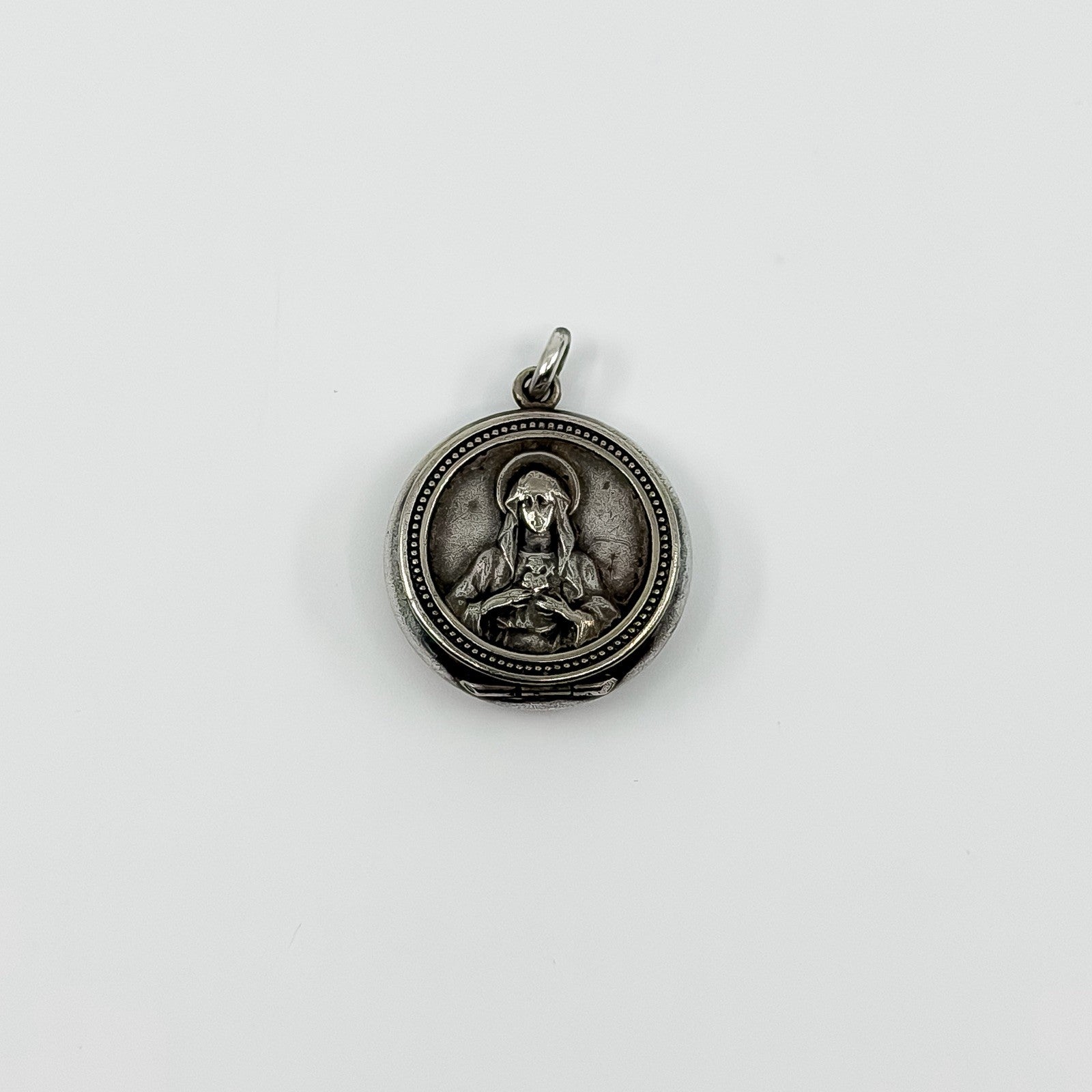 Vintage sterling silver Virgin Mary Christian photo locket pendant with jump ring on white background.