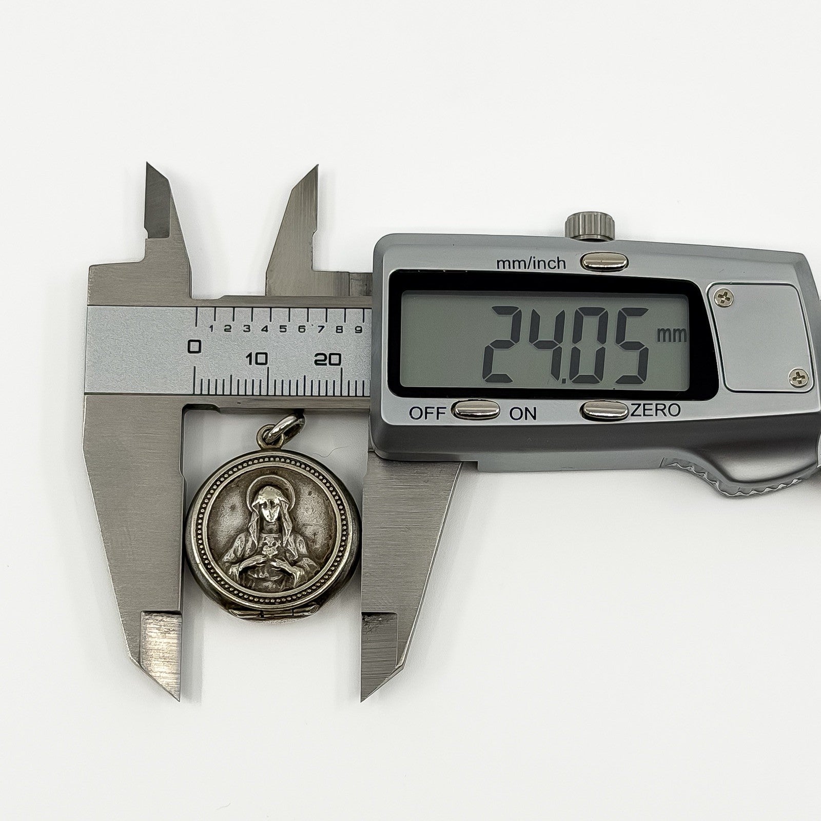 Digital caliper measuring the vintage sterling silver Virgin Mary locket pendant at approximately 24.05mm.