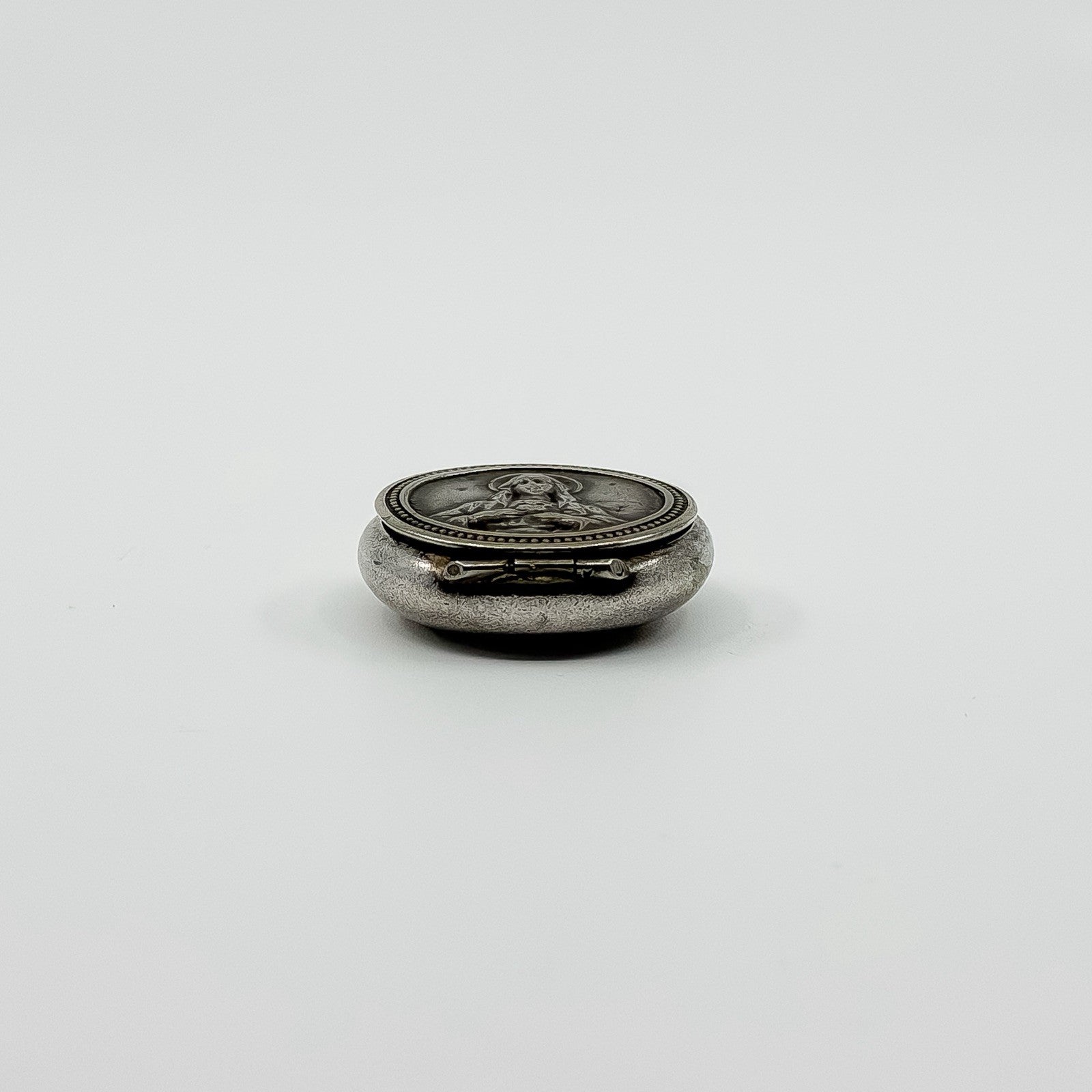 Side view of vintage sterling silver Virgin Mary photo locket showing the hinge and rounded case.