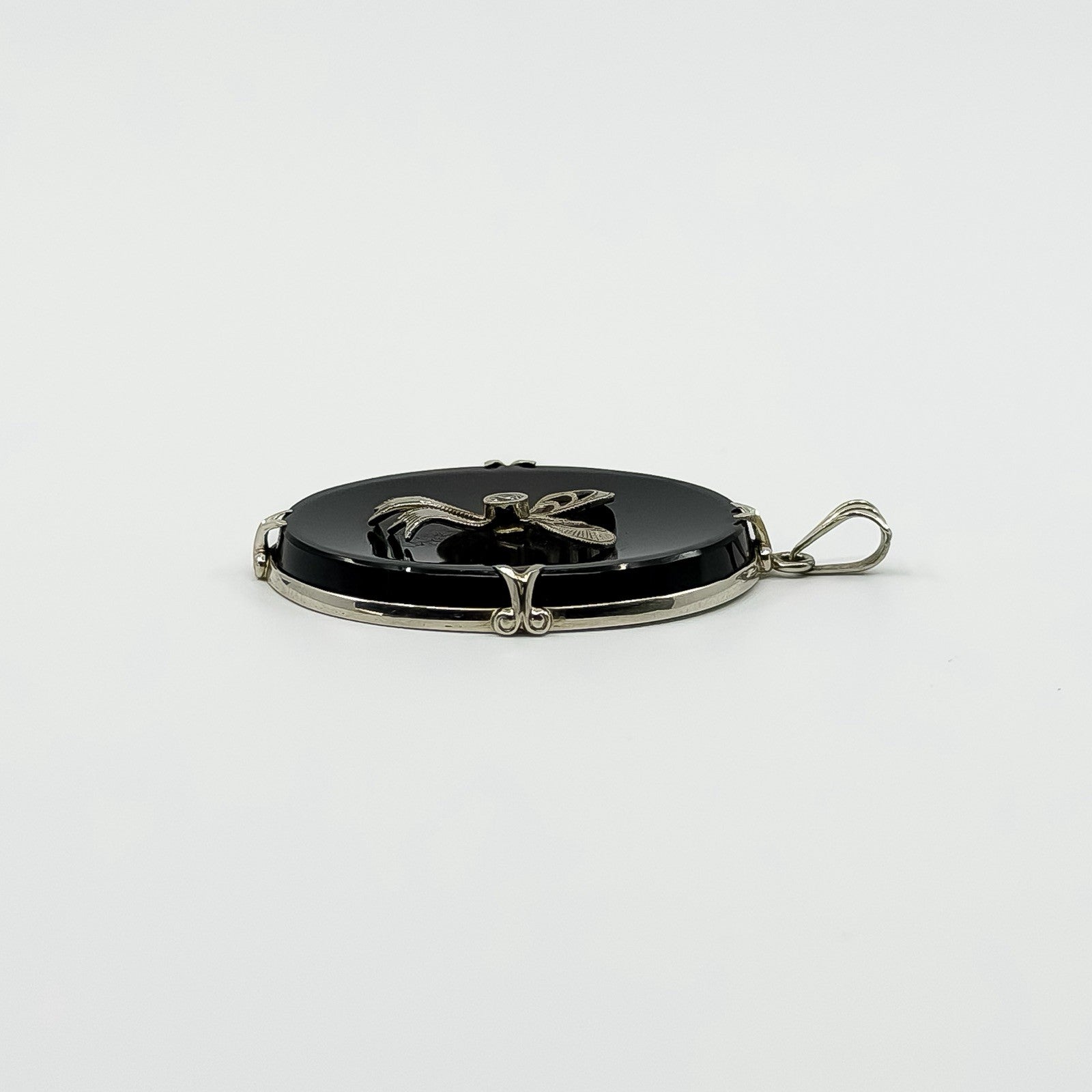Side view of vintage black onyx bow pendant showing the white gold frame and bail.