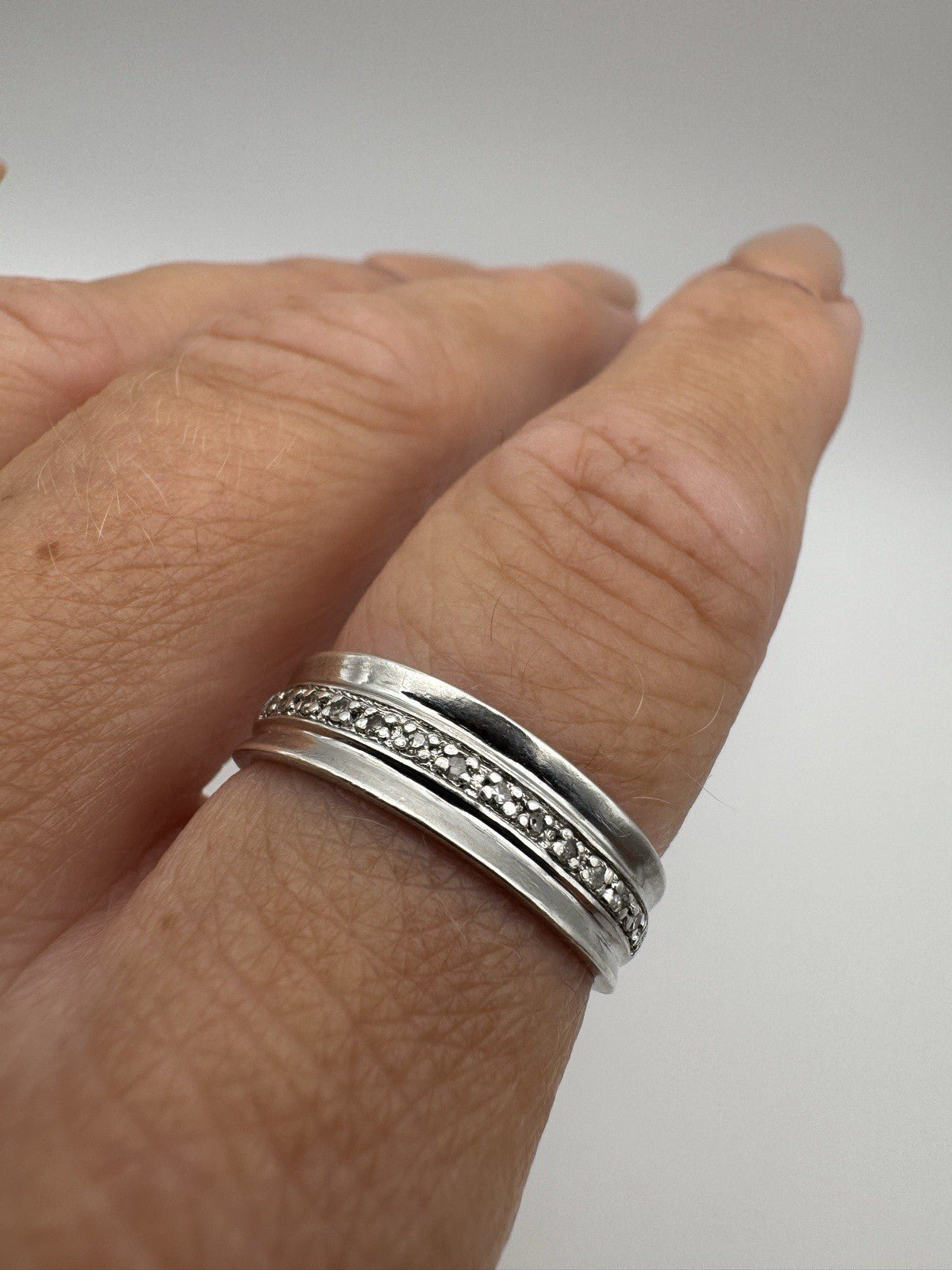 Sterling silver half hoop diamond band worn on hand, side profile view