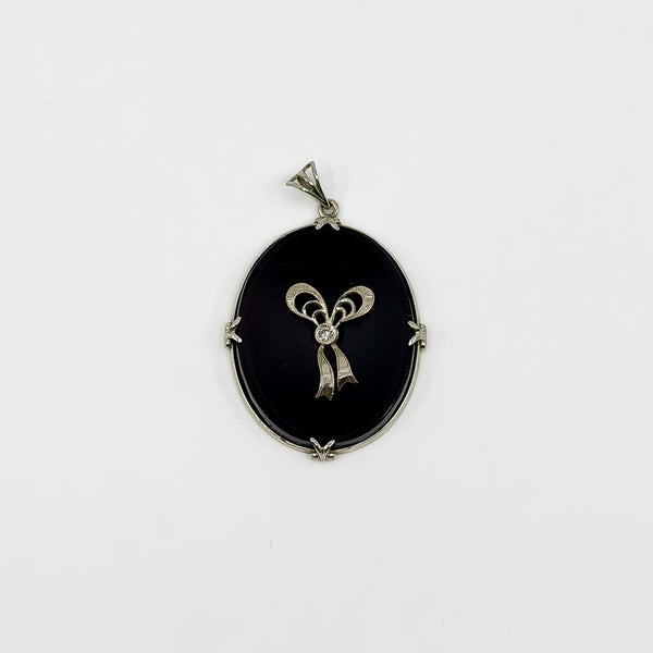 Vintage 14ct white gold black onyx pendant with diamond bow centre on white background.
