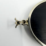 Close up of the 14k stamp on the white gold bail of the black onyx and diamond bow pendant.