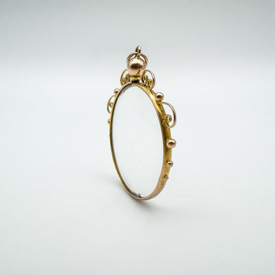 Angled standing view of antique double-sided glass locket pendant in 9ct gold.