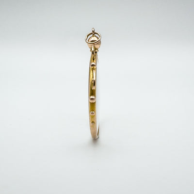 Narrow edge view of antique gold locket pendant with clear glass panels.