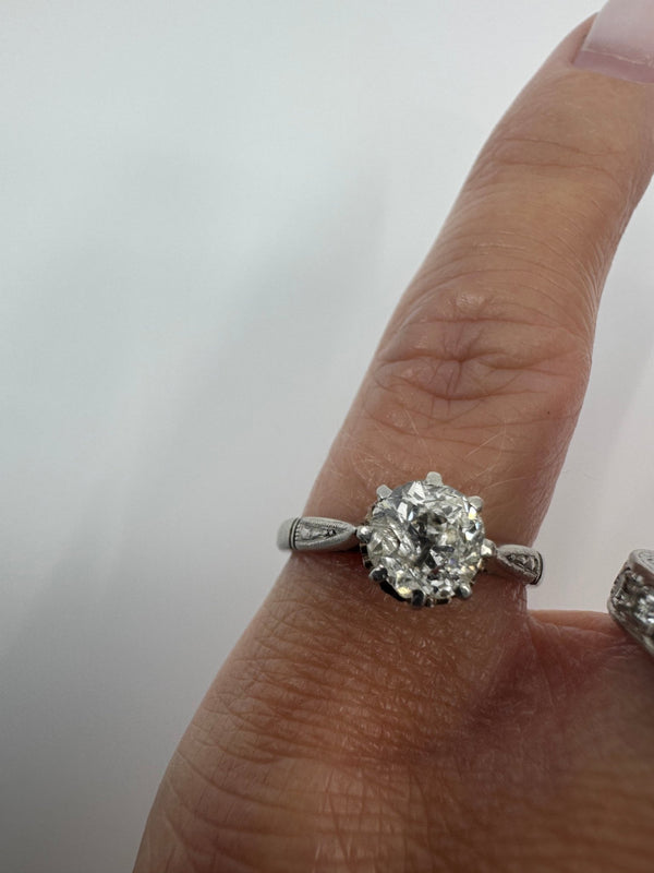 Antique platinum old-cut diamond solitaire ring worn on the finger with engraved shoulders visible