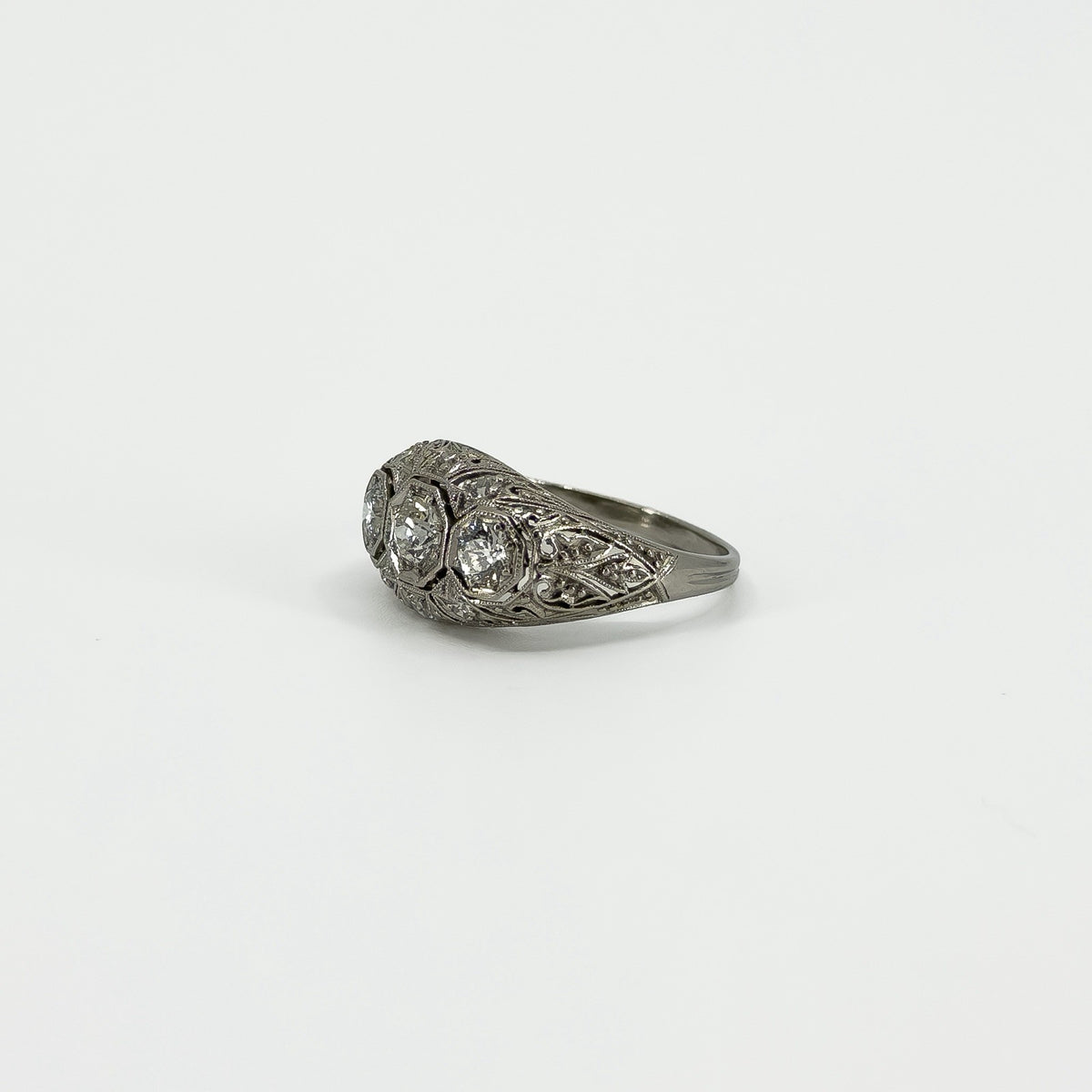 Angled side view of Art Deco platinum diamond trilogy ring with filigree detail