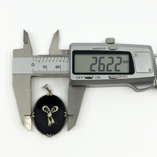 Digital caliper measuring the black onyx and diamond bow pendant width at approximately 26.22mm.