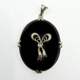 Close up of vintage 14ct white gold black onyx pendant with bow design and centre diamond.